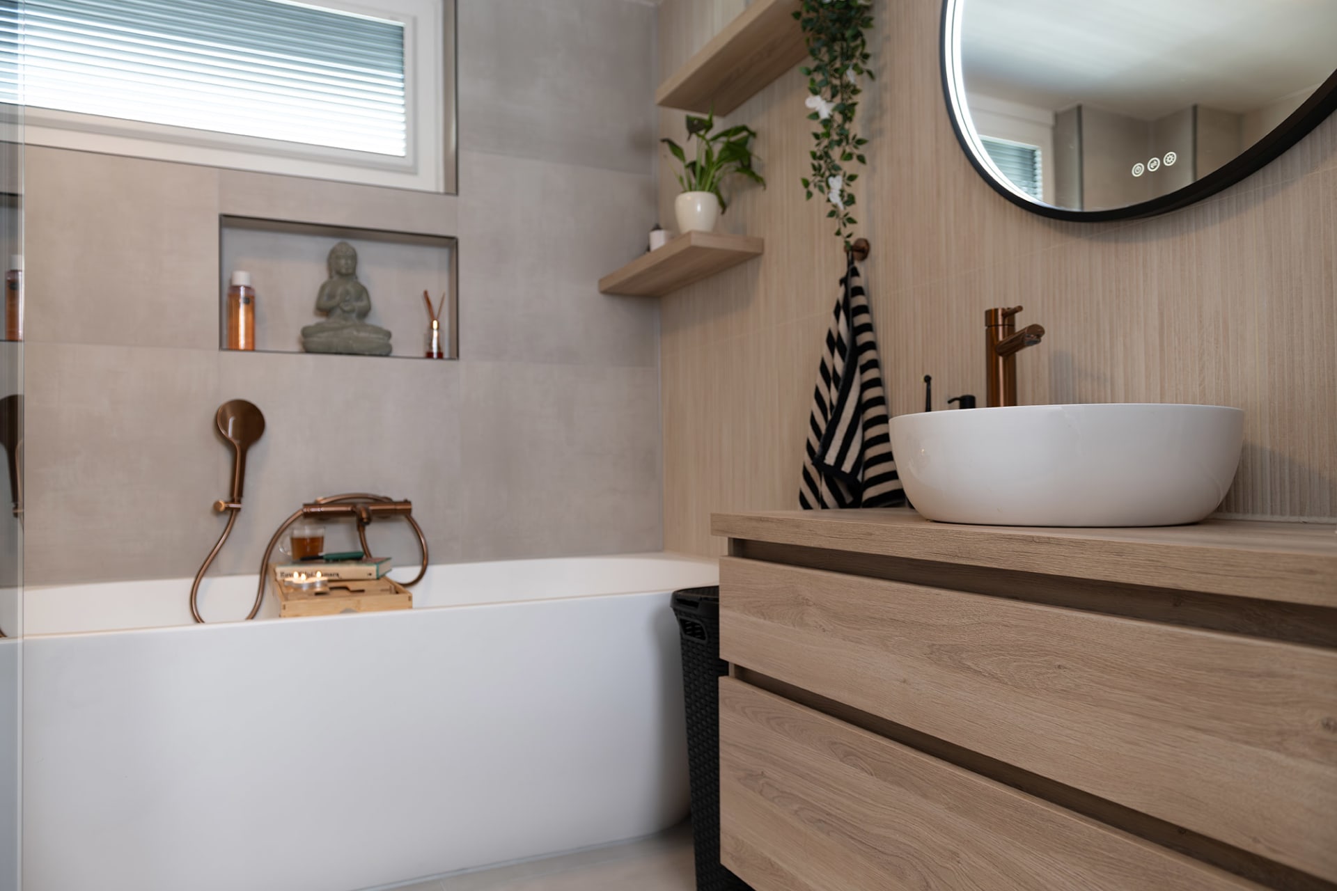 Complete lichte badkamer met ligbad, houten meubel en ronde spiegel