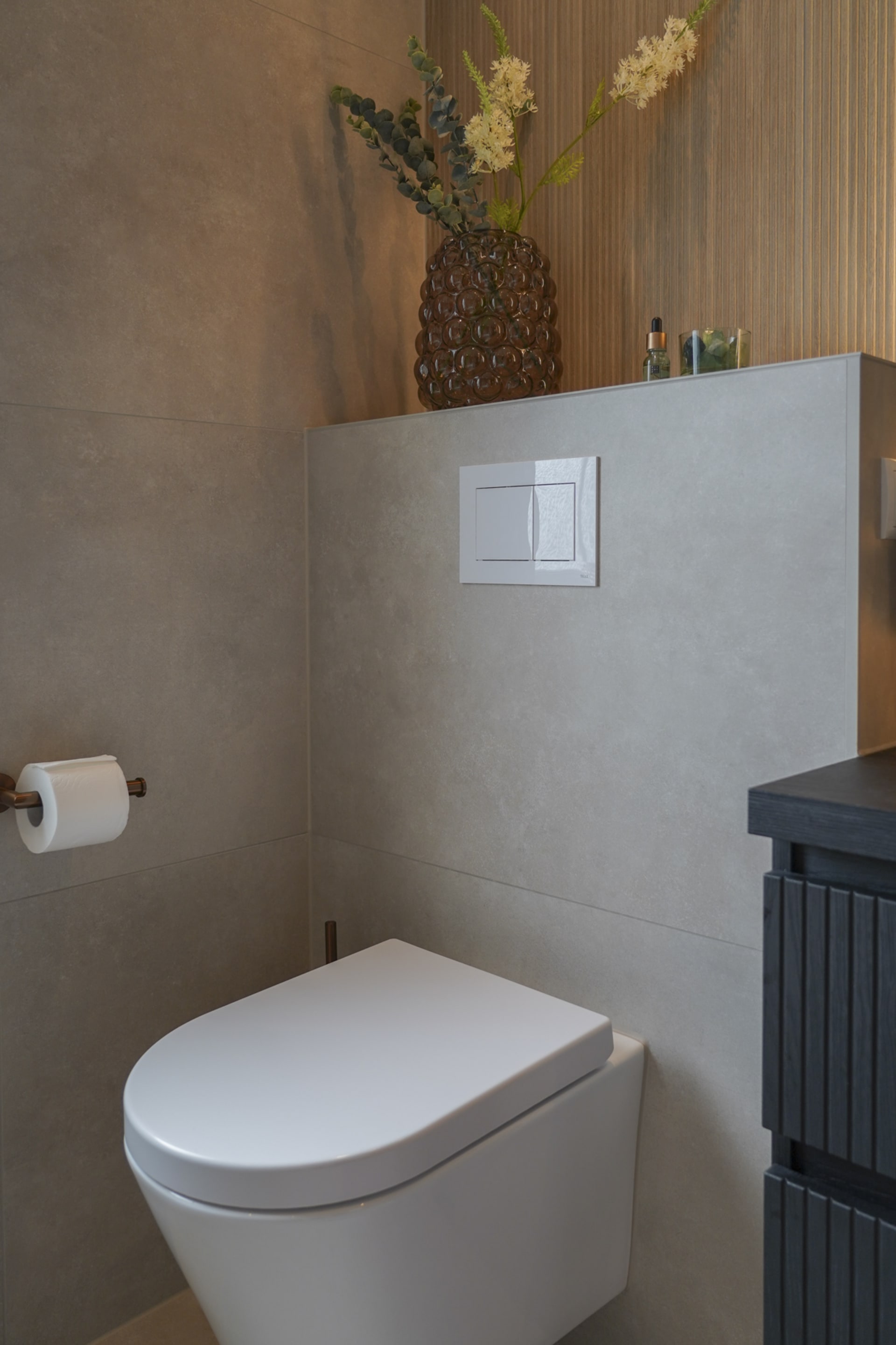 Hangend toilet met koperen rolhouder tegen betonlook tegels