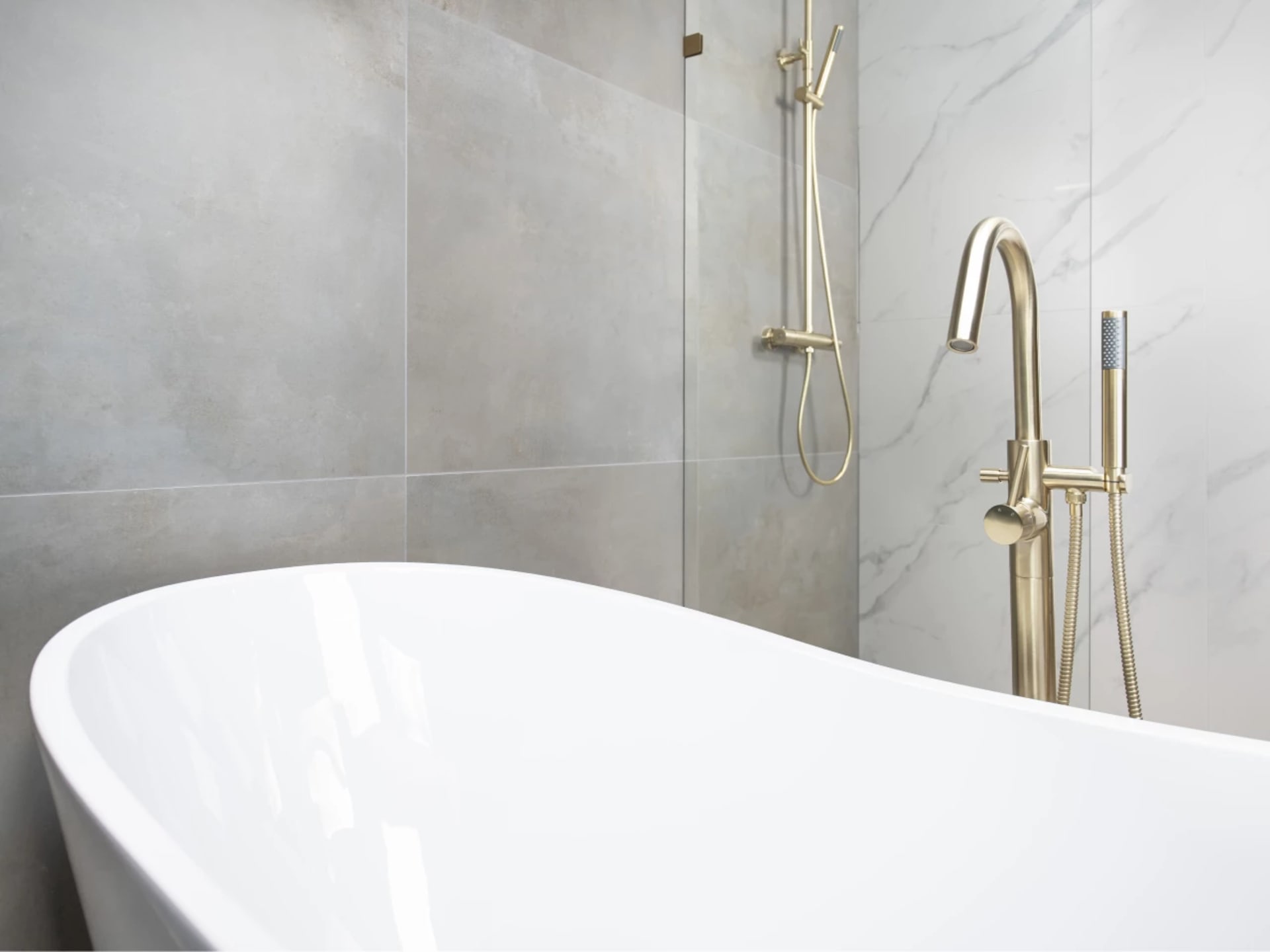 Wit vrijstaand bad met een vrijstaande badkraan en handdouche in geborsteld goud tegen de betonlook wand