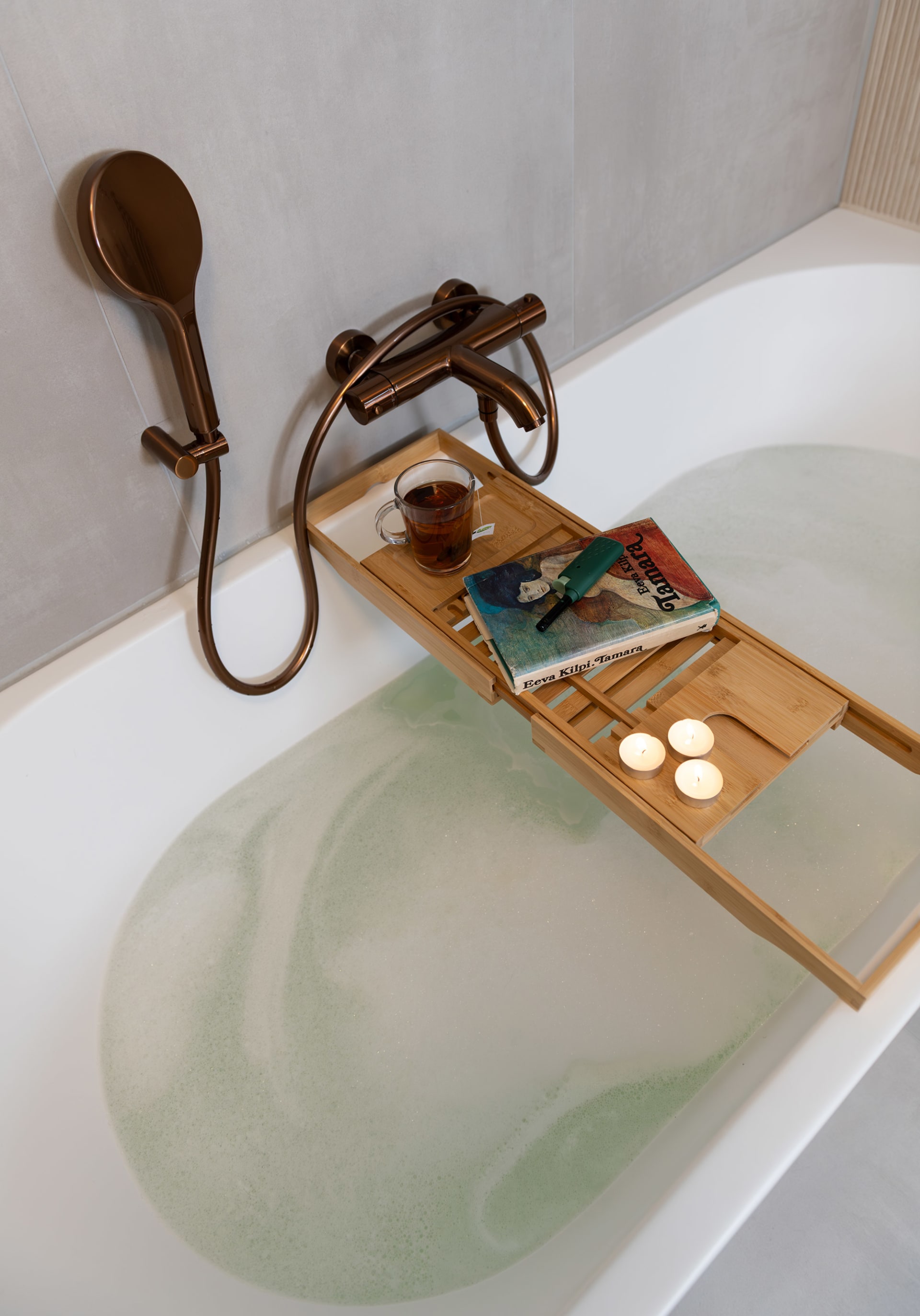 Bad met schuimend water en een bamboe badplank met een kop thee, een boek en drie brandende waxinelichtjes