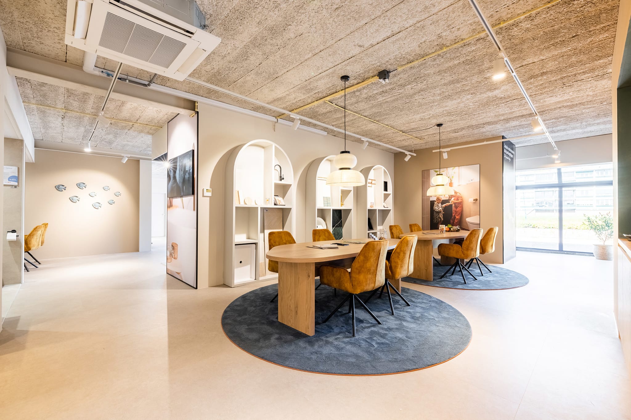 Ruime Sani4All winkel met twee ovale houten vergadertafels en diverse badkameropstellingen.
