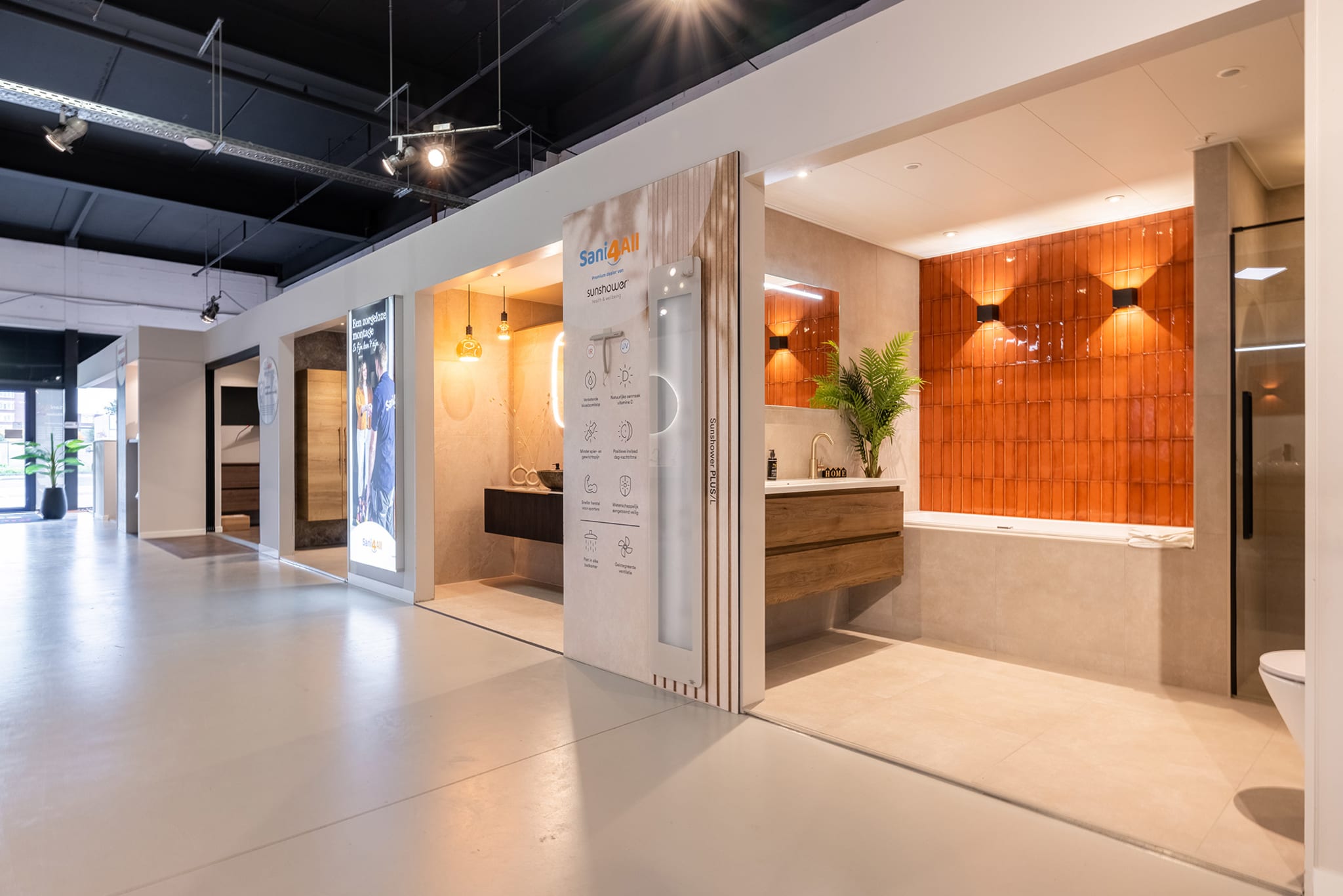 Badkameropstellingen in de winkel van Sani4All Hoogeveen, met een bad voor een wand van oranje tegels