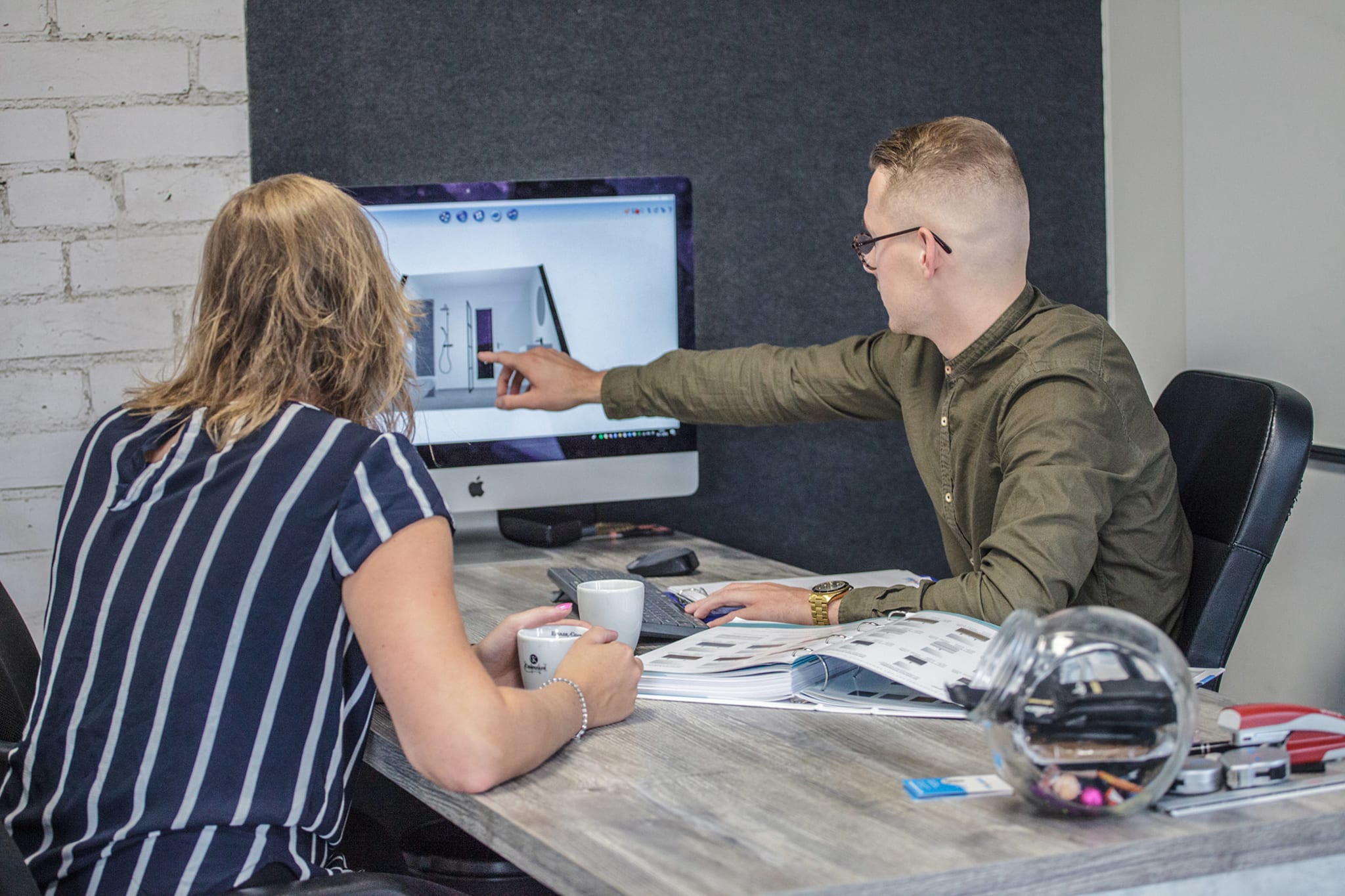 Twee mensen bespreken een badkamerontwerp op een computerscherm tijdens een adviesgesprek