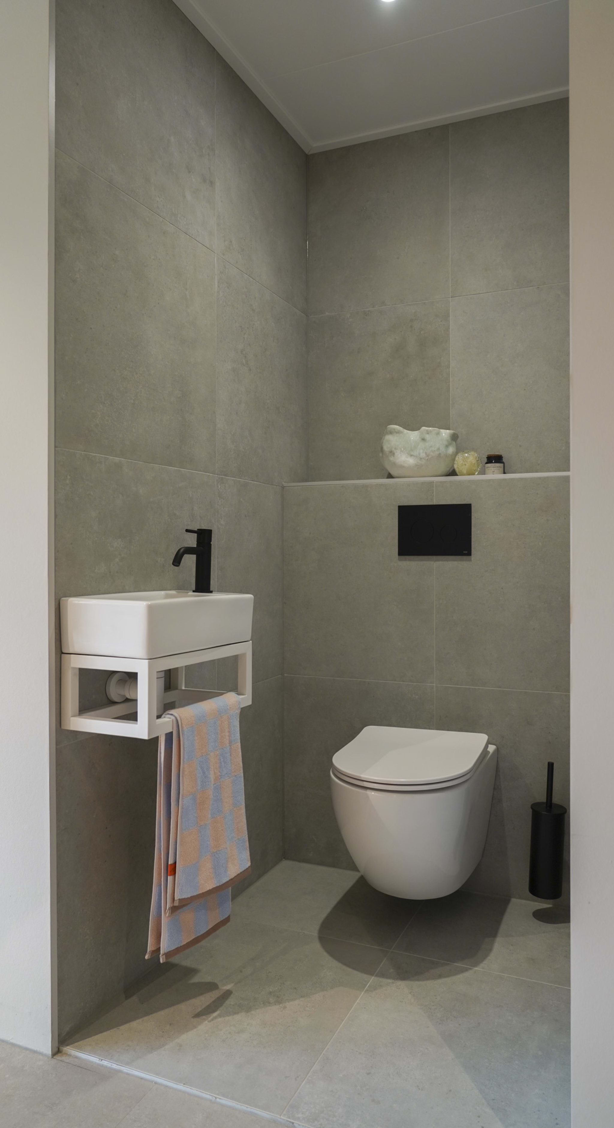 Grijze toiletruimte met wandcloset, wit fonteintje met zwarte kraan en bijpassende accessoires.