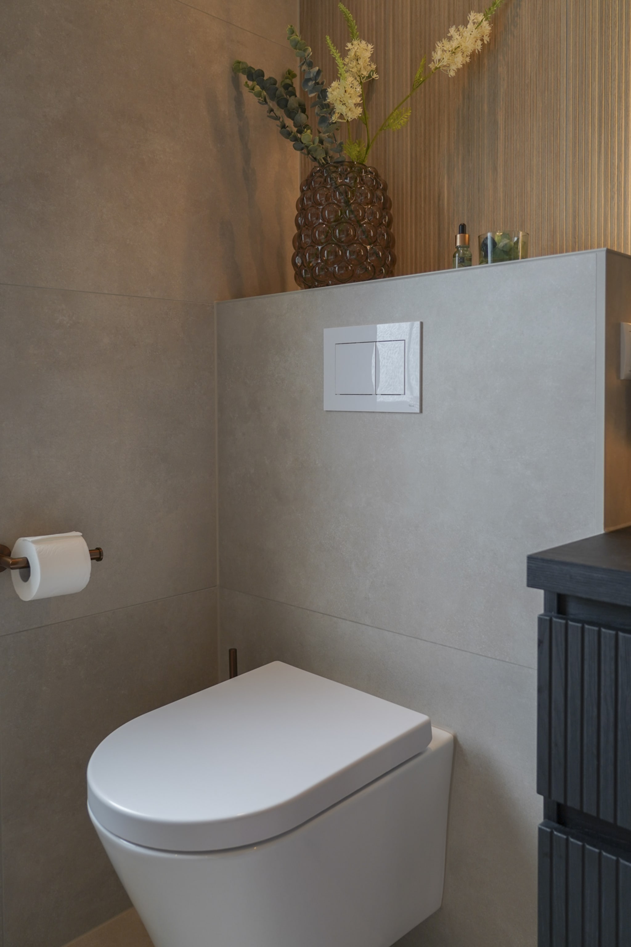 Hangend toilet met koperen rolhouder tegen betonlook tegels