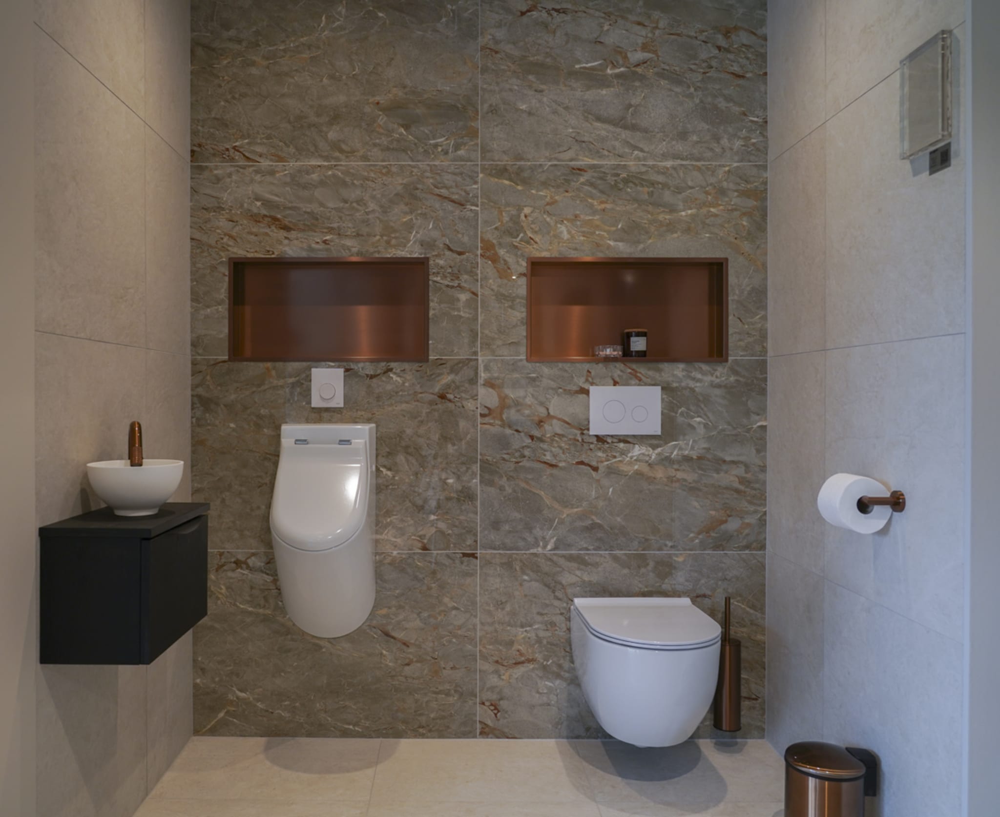 Een toiletruimte met een marmerlook achterwand, een toilet, urinoir en een fonteintje met zwarte onderkast.