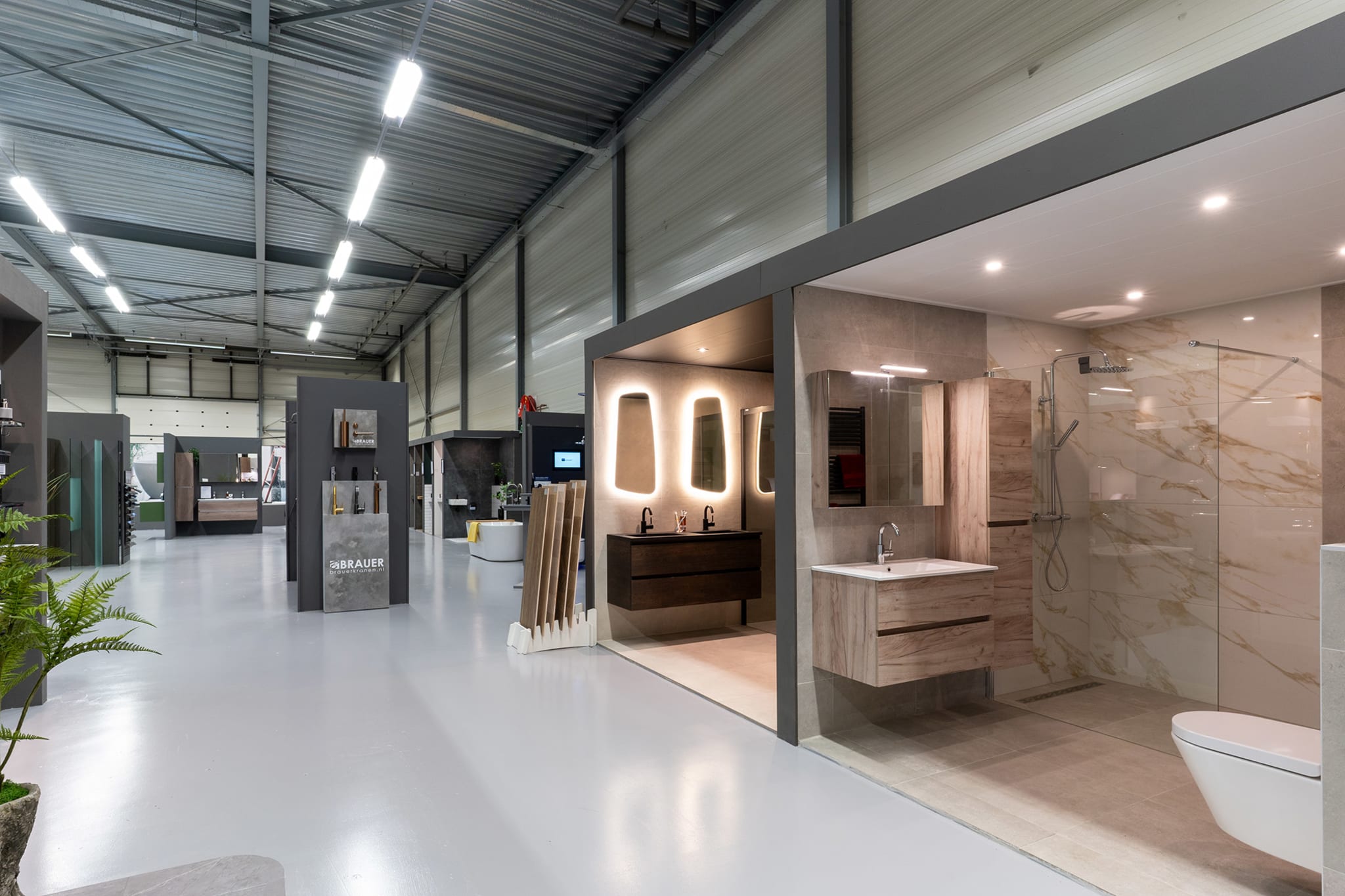 Overzicht van de Sani4All winkel met diverse badkameropstellingen, waaronder een moderne badkamer met houtlook meubels en marmeren tegels.