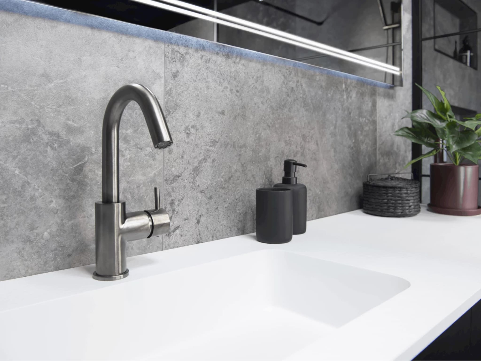 Close-up van de wastafelkraan in Brushed Graphit op het mat witte blad van Solid Stone, met de ledverlichting van de spiegel erboven