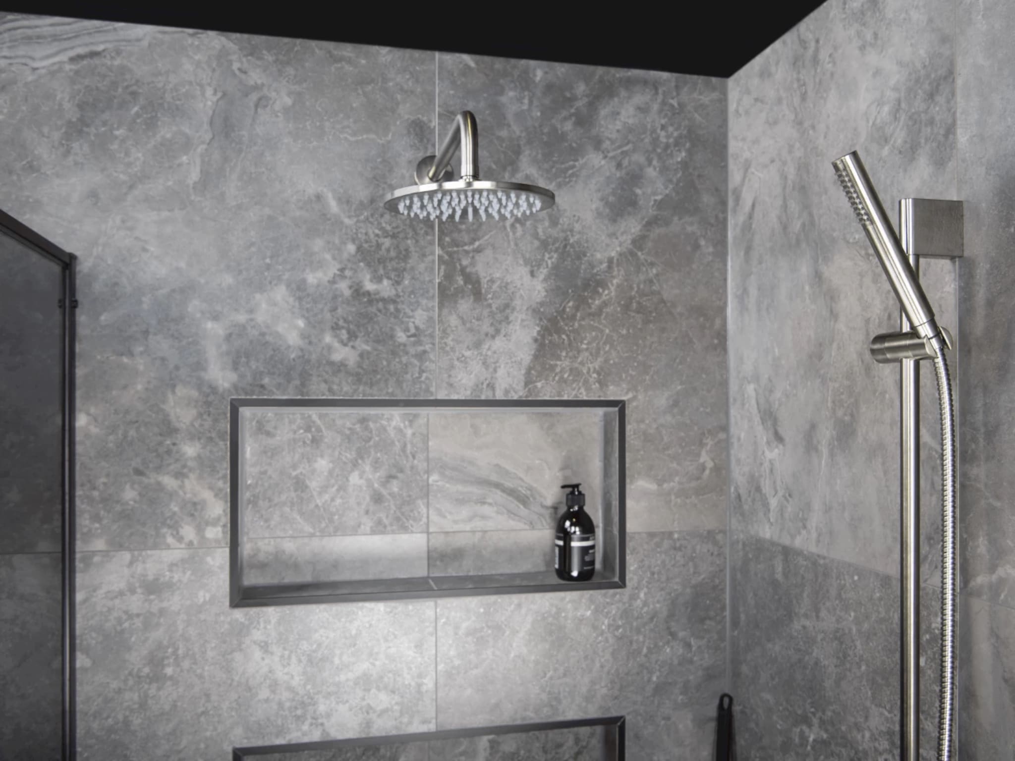 Ronde regendouche in Brushed Graphit met losse handdouche aan een glijstang, naast een nis in de gemarmerde tegelwand