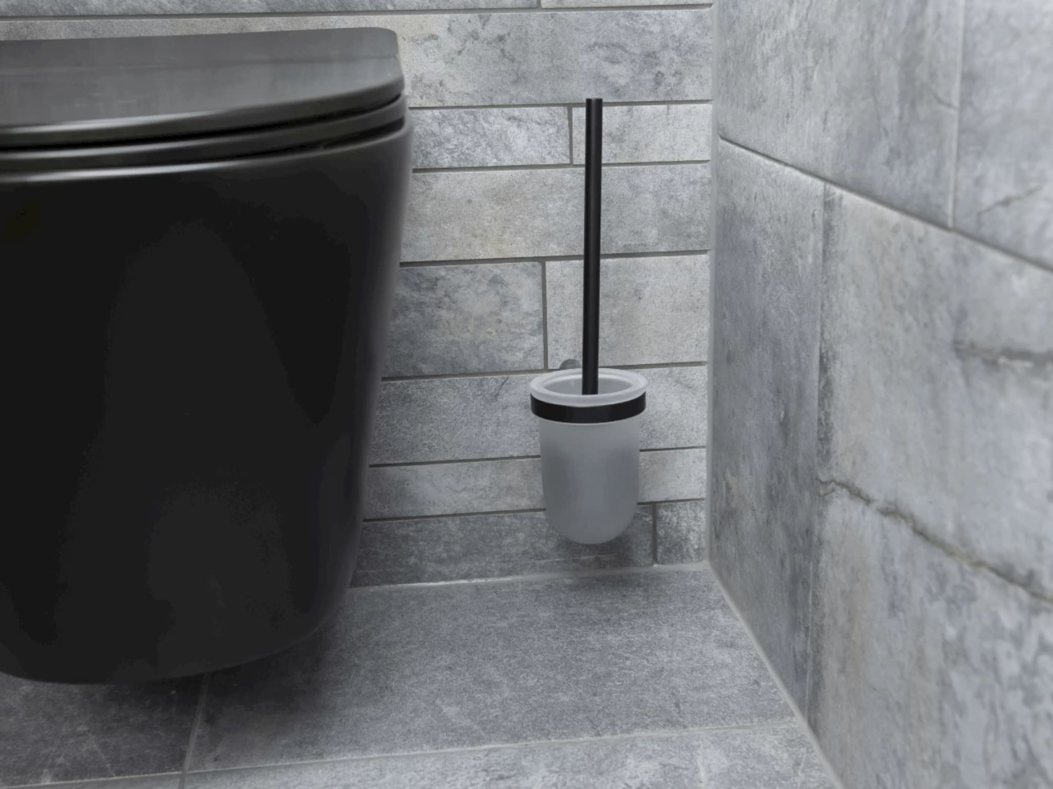 Close-up van het zwarte wandcloset met een zwarte toiletborstelhouder tegen de grijze strooktegels