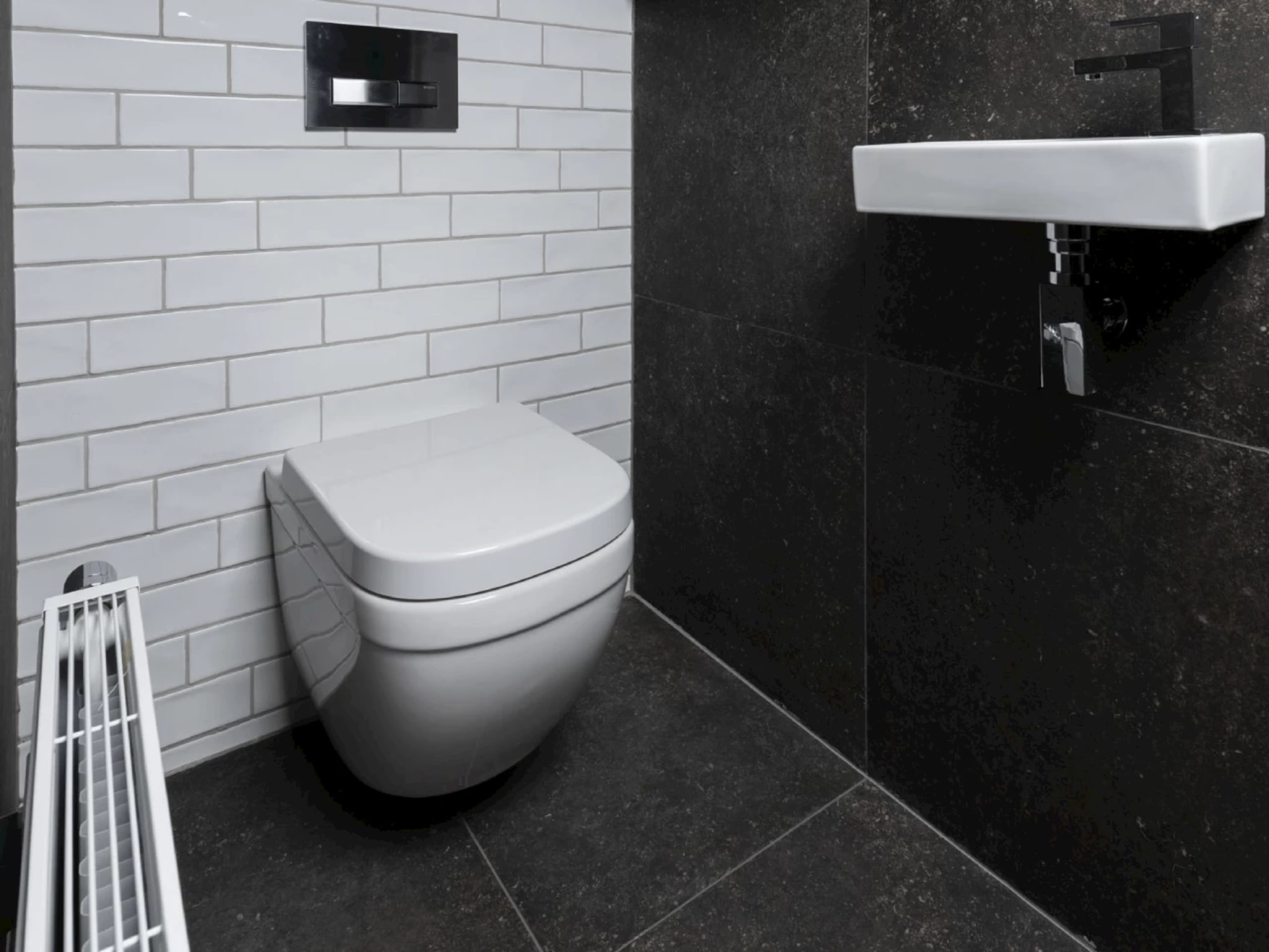 Hoekaanzicht met de witte keramische fontein tegen de donkere terrazzolook wand en het wandcloset links