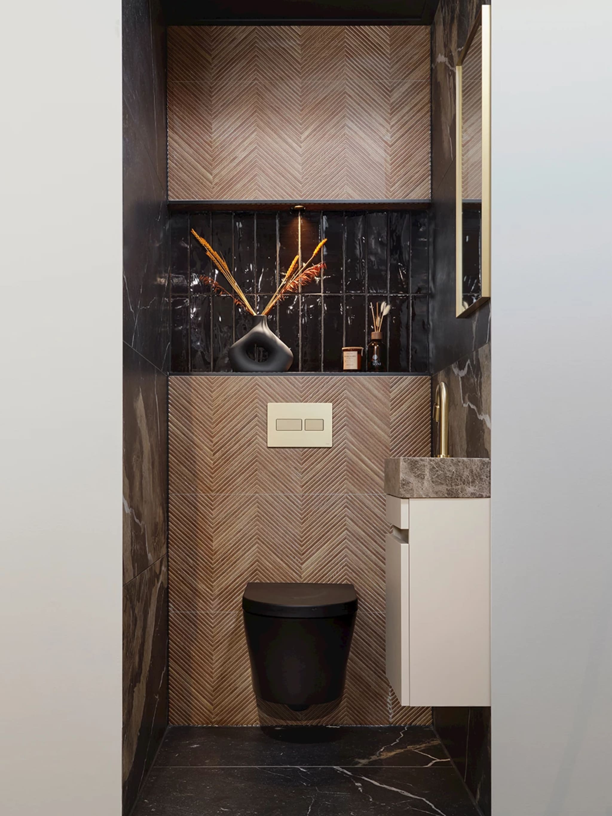 De hele toiletruimte van voren, met de visgraatwand, de zwarte nis en de donkere marmerlook vloer