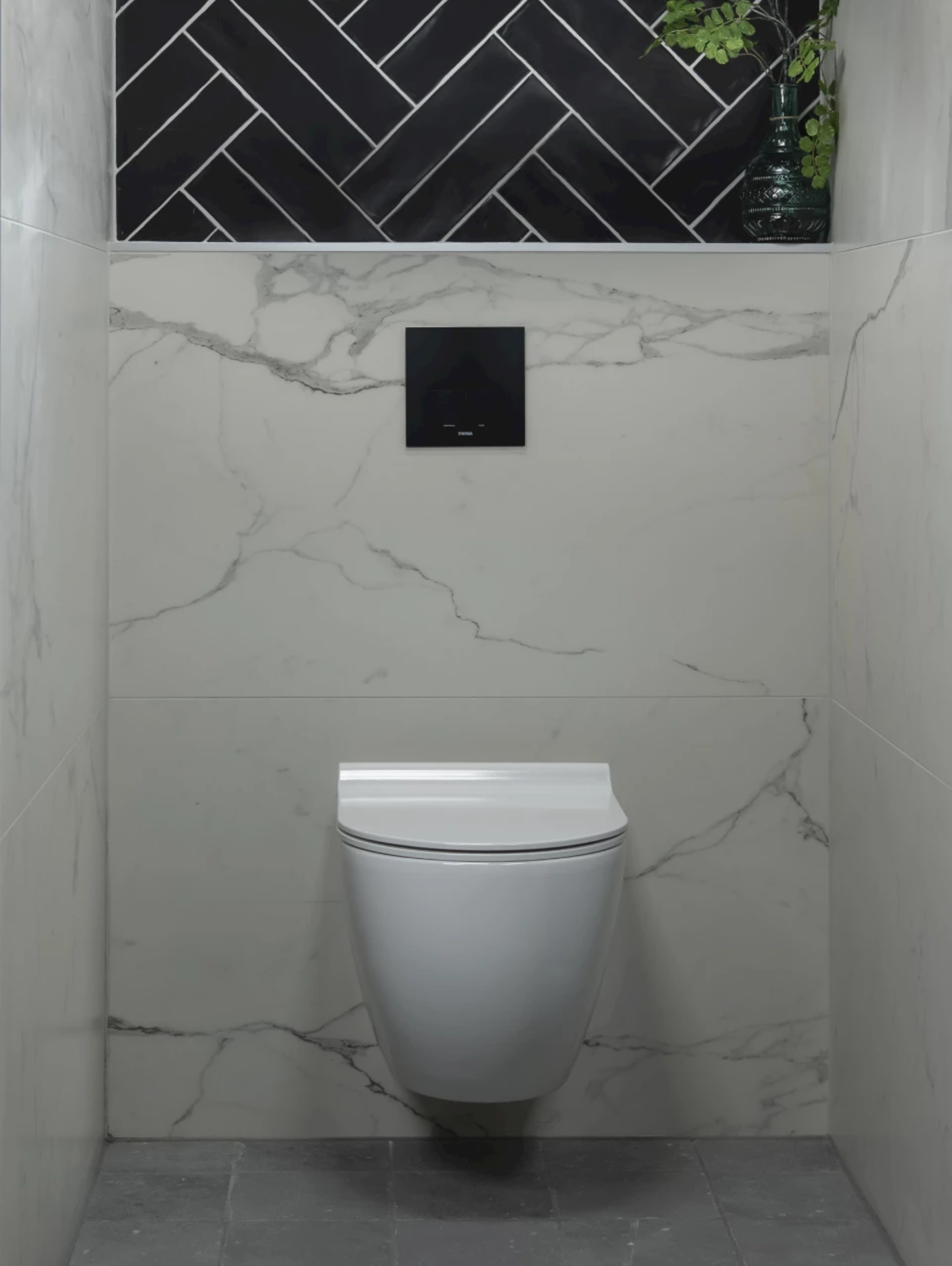 Compleet toilet Modern Thirties met witte marmerlook wandtegels, een band zwarte visgraattegels en een wit randloos wandcloset