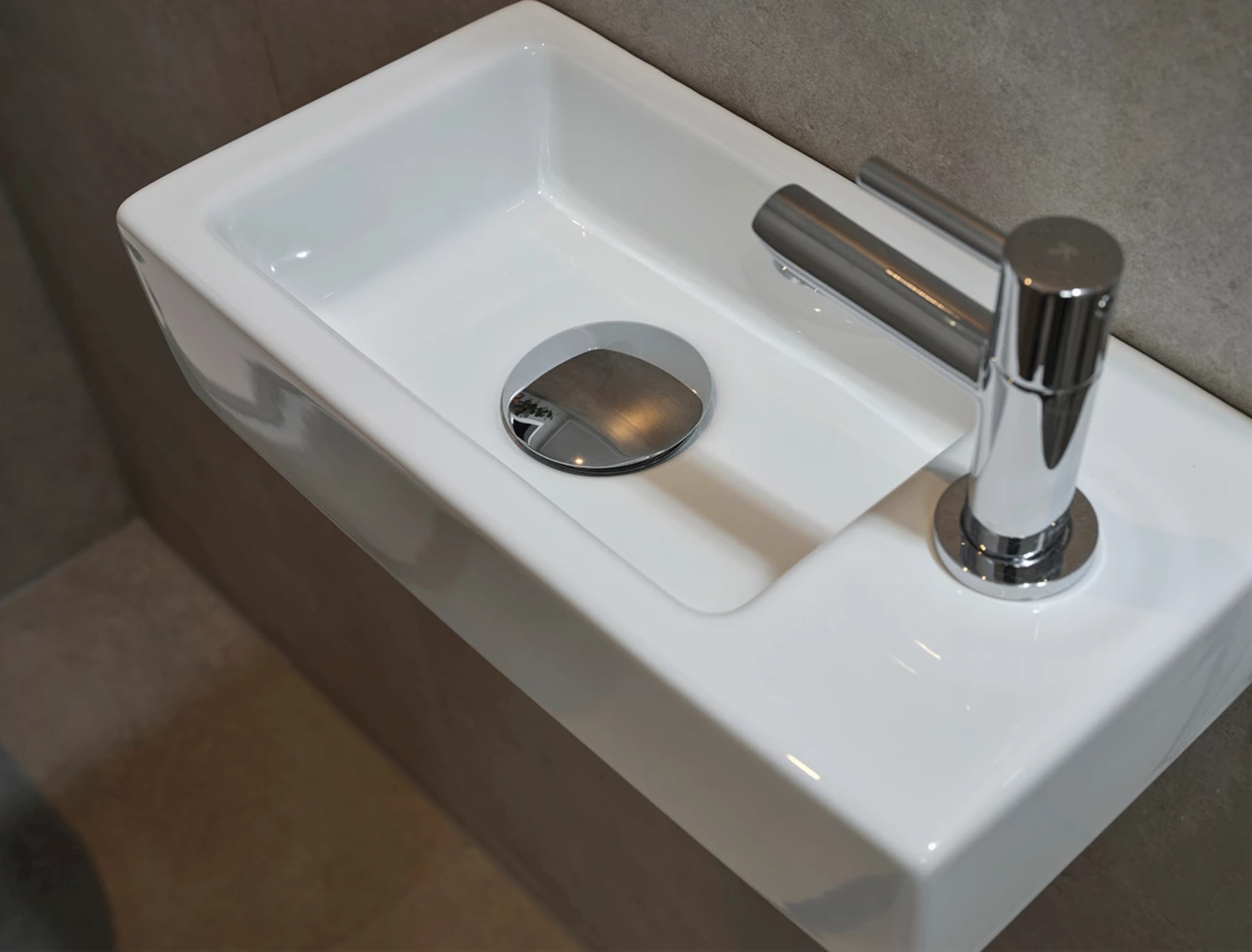 Het witte fonteintje van bovenaf, met de chromen plug in de bak en de chromen kraan aan de zijkant