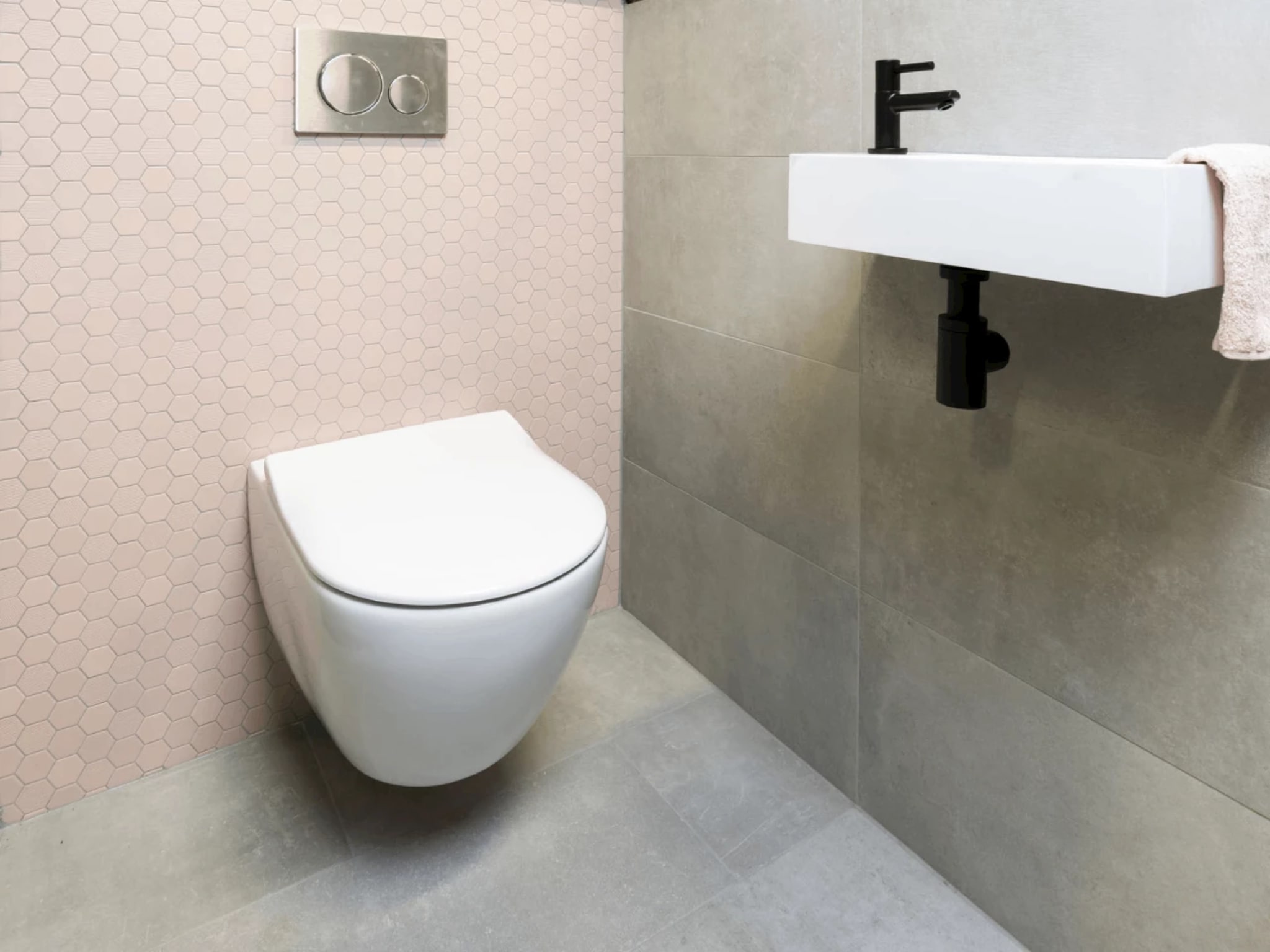Mat witte fontein met een mat zwarte kraan en zwarte sifon aan de grijze betonlook wand, naast de roze hexagonwand