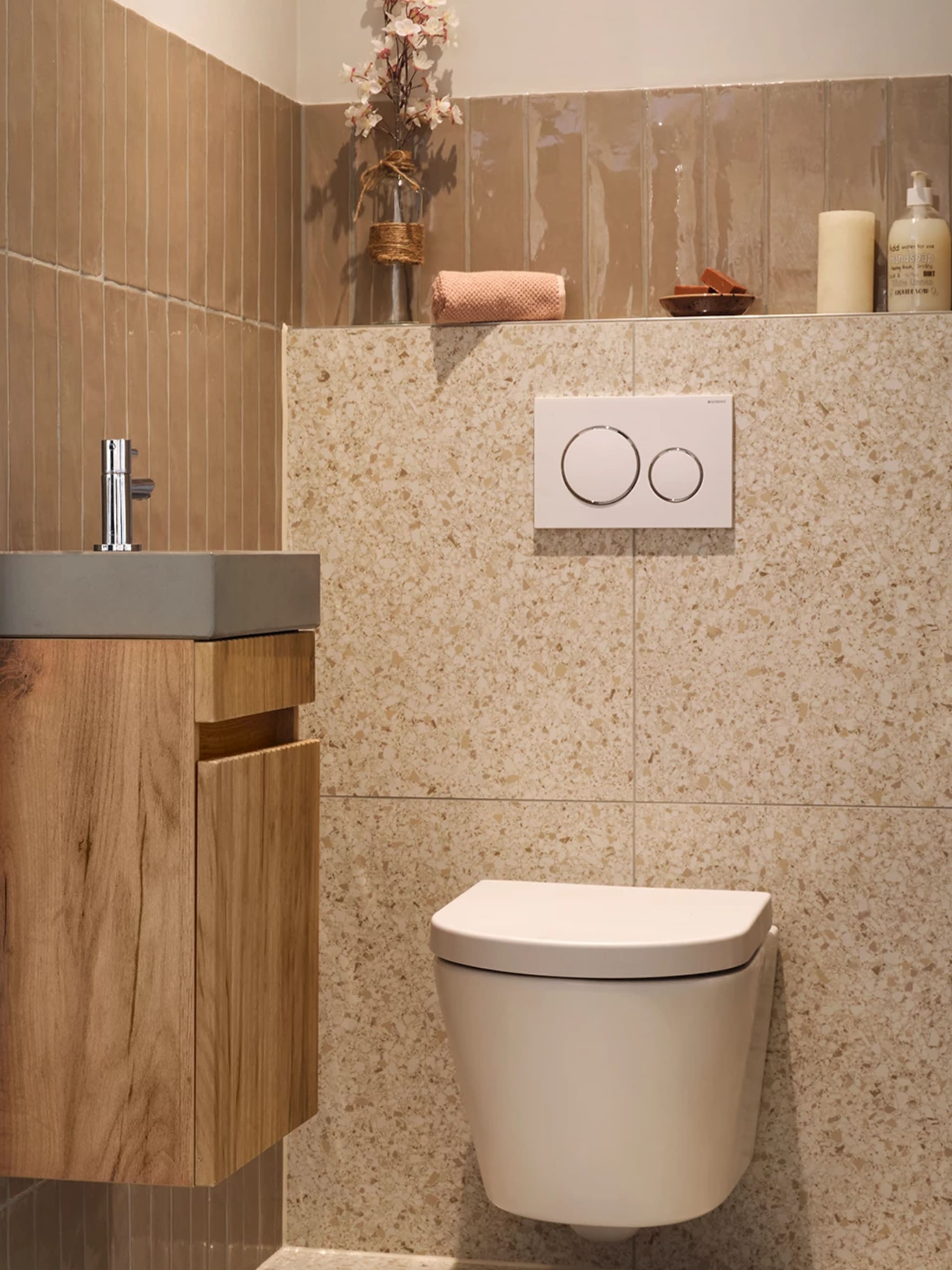 Beige terrazzotegels met warme spikkels en een bedieningspaneel met chromen ringen bij Sani4All