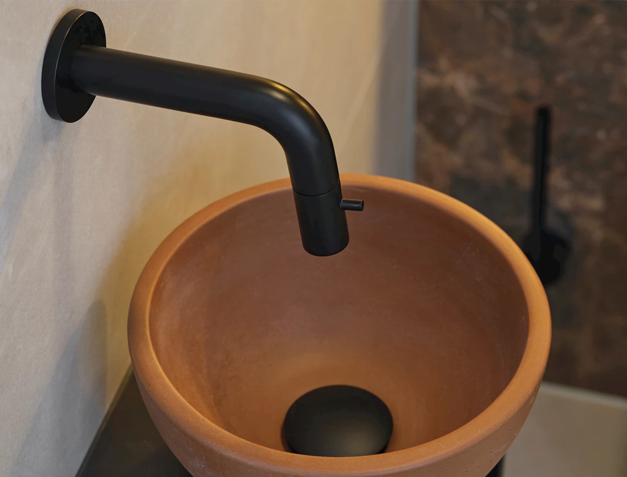 Close-up van de ronde terracotta fonteinkom met een mat zwarte inbouwkraan erboven