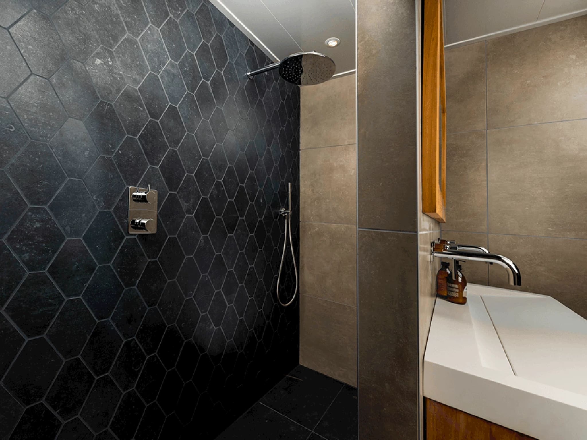 Inloopdouche met chromen regendouche en losse handdouche tegen de wand met zwarte hexagontegels