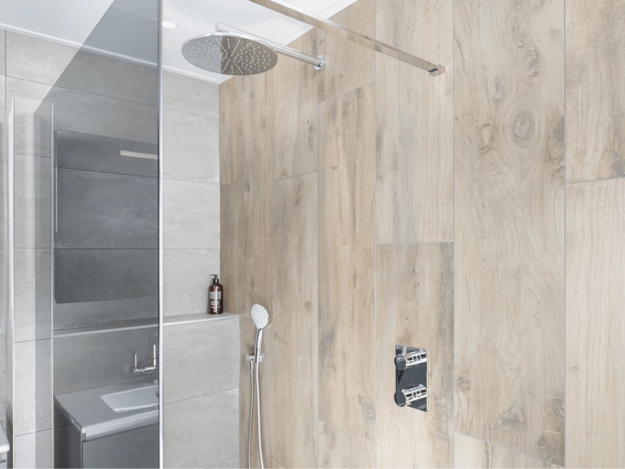 Chromen regendouche en losse handdouche tegen de houtlook wandtegels van de inloopdouche