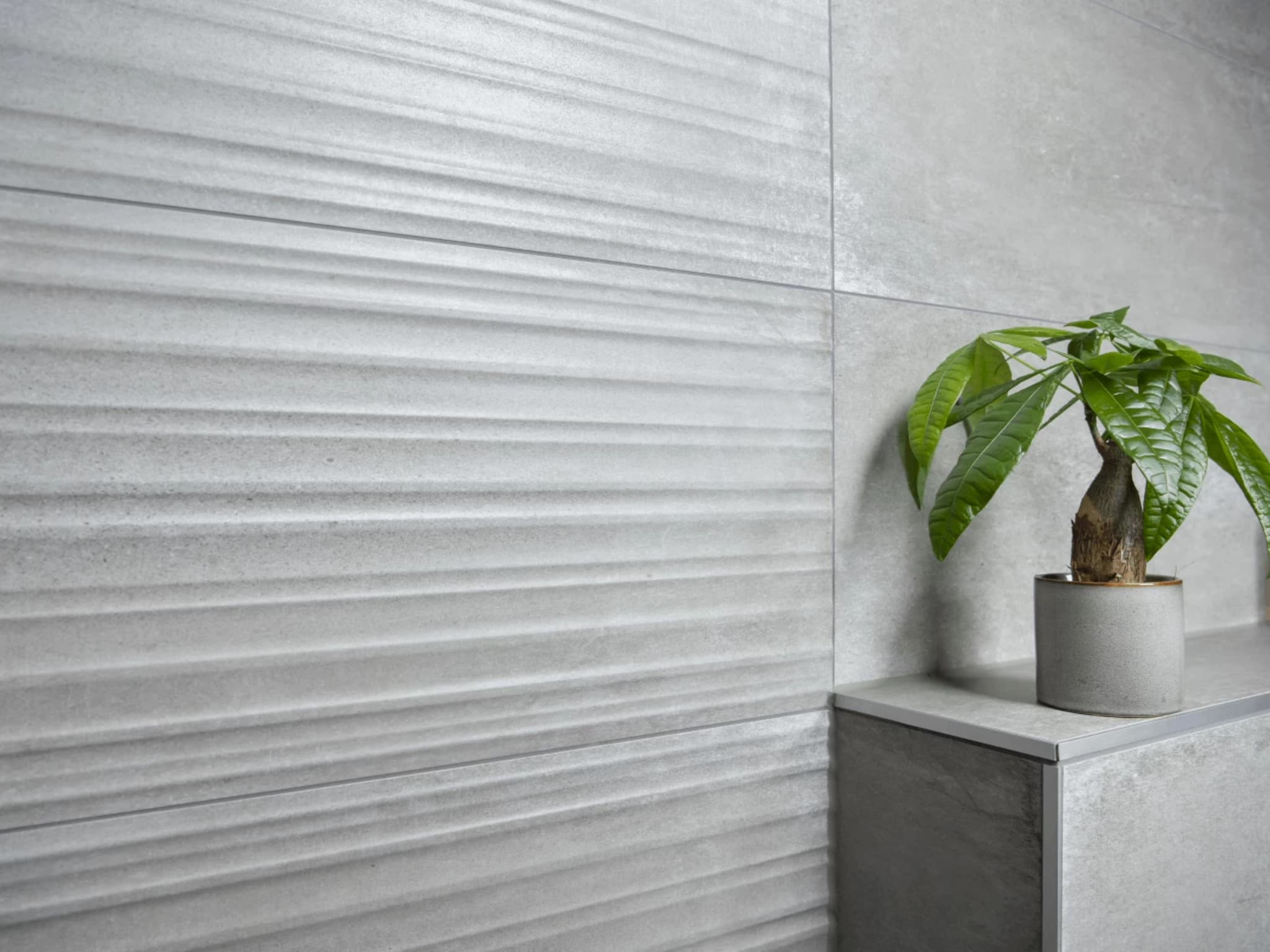 Close-up van de grijze decortegels met geribbeld reliëf naast de gladde betonlook wandtegels