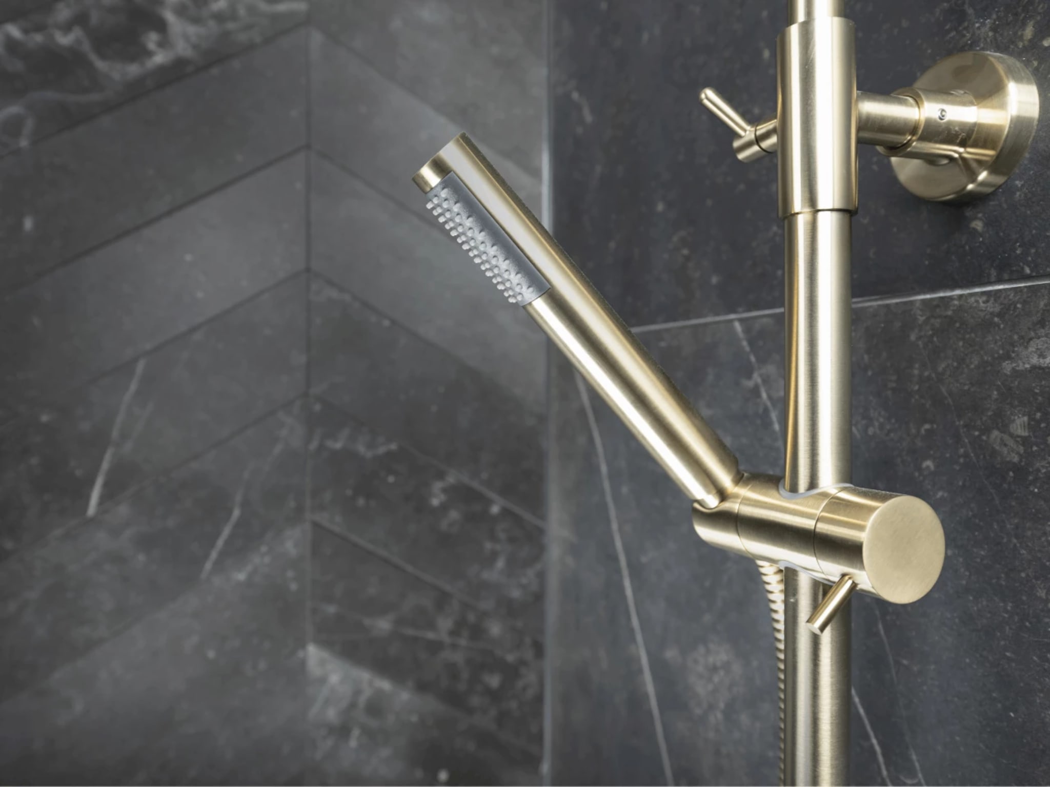 Close-up van de handdouche en de bediening in geborsteld goud tegen de donkere marmerlook tegels