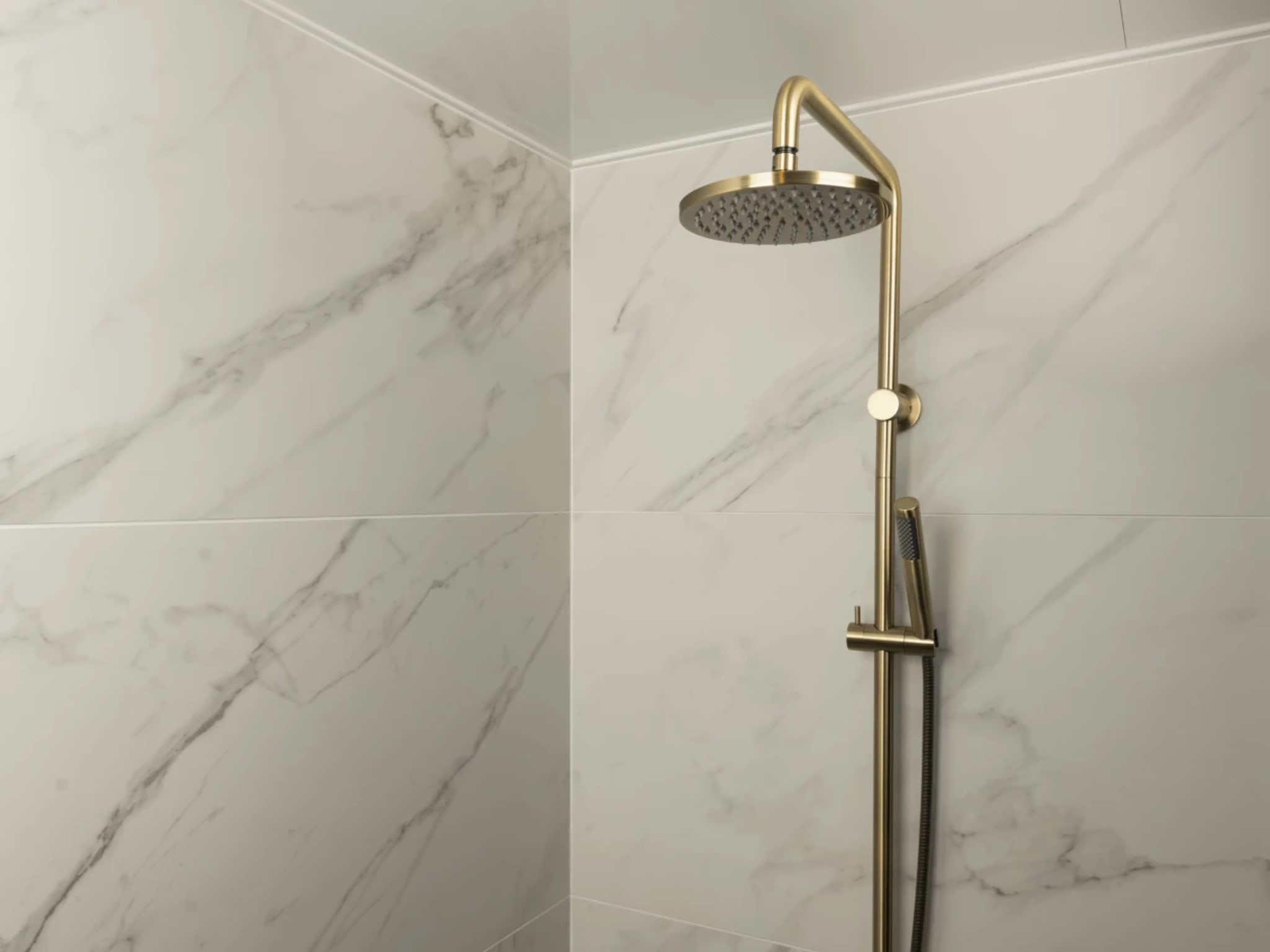Regendoucheset met losse handdouche in geborsteld goud tegen de marmerlook wandtegels van de doucheruimte
