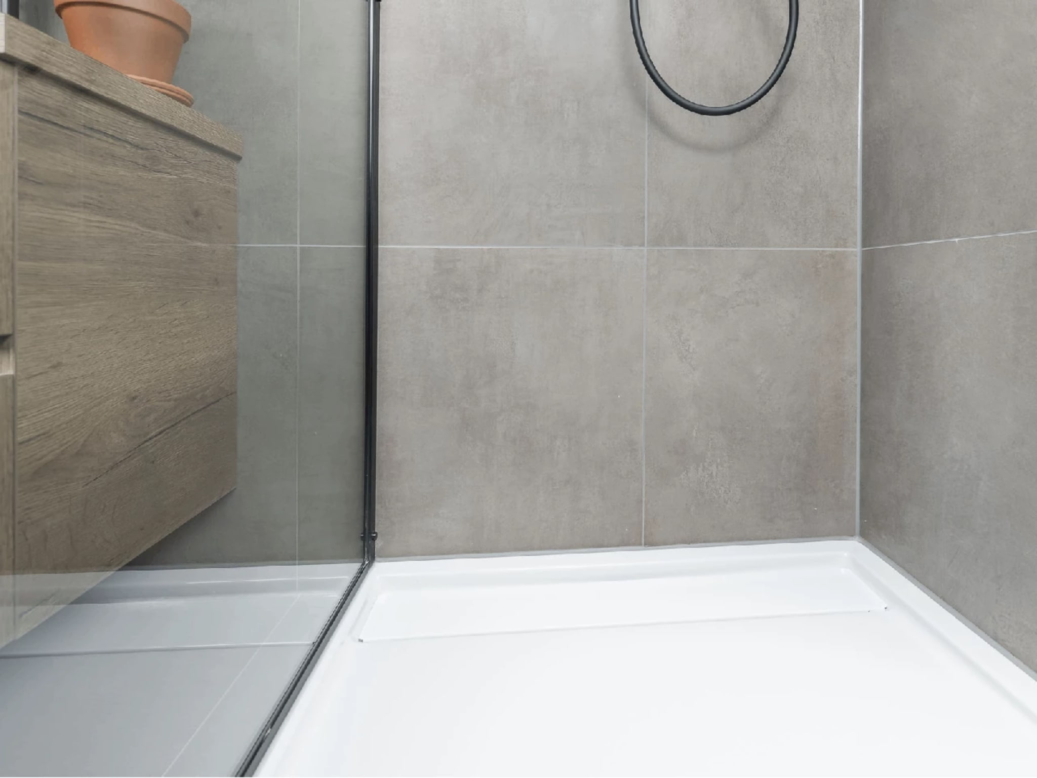 Witte douchebak achter de glazen douchewand met mat zwart profiel, met links het houtlook badmeubel