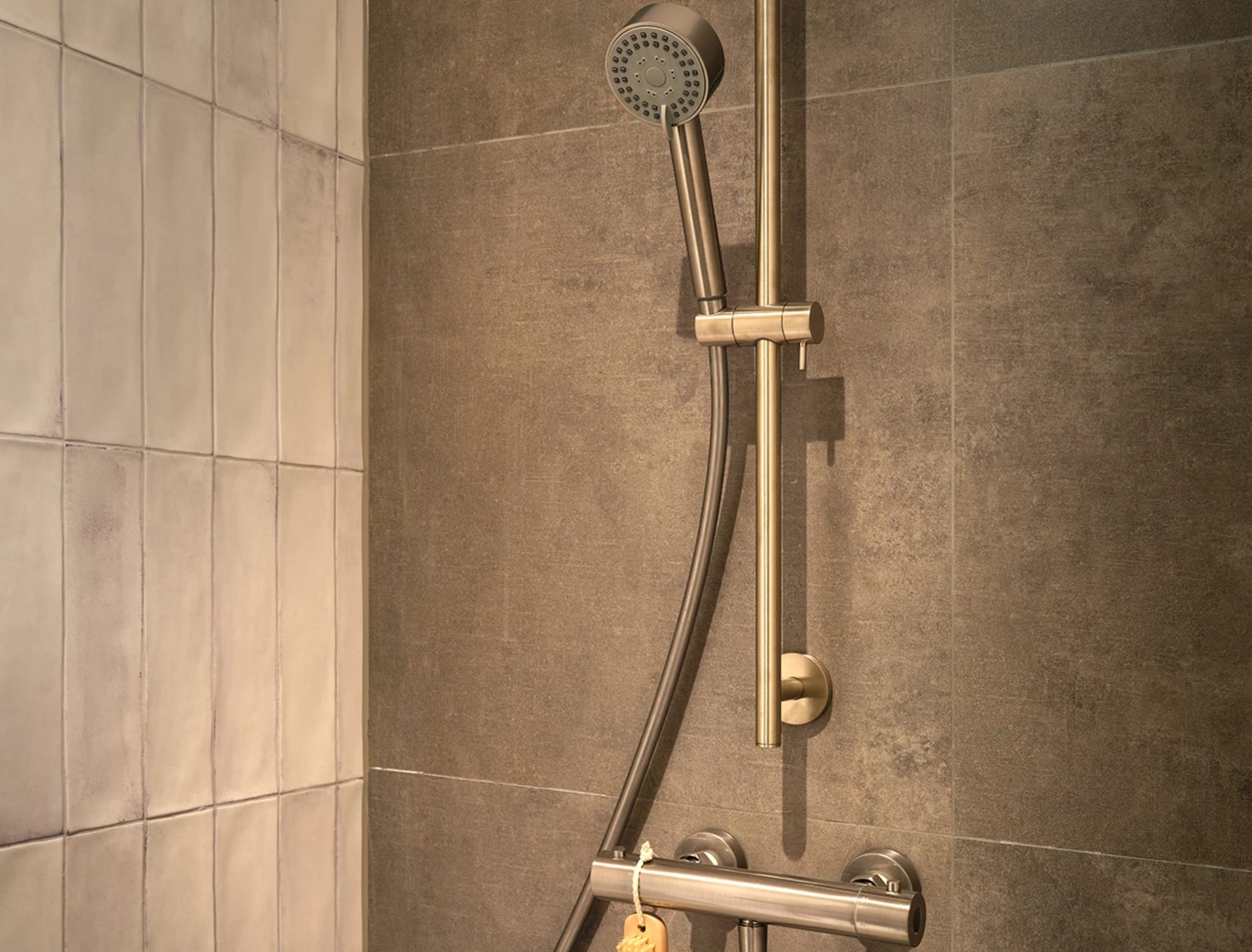 Handdouche op een glijstang met thermostaatkraan in geborsteld staal tegen de grijze betonlook wandtegels