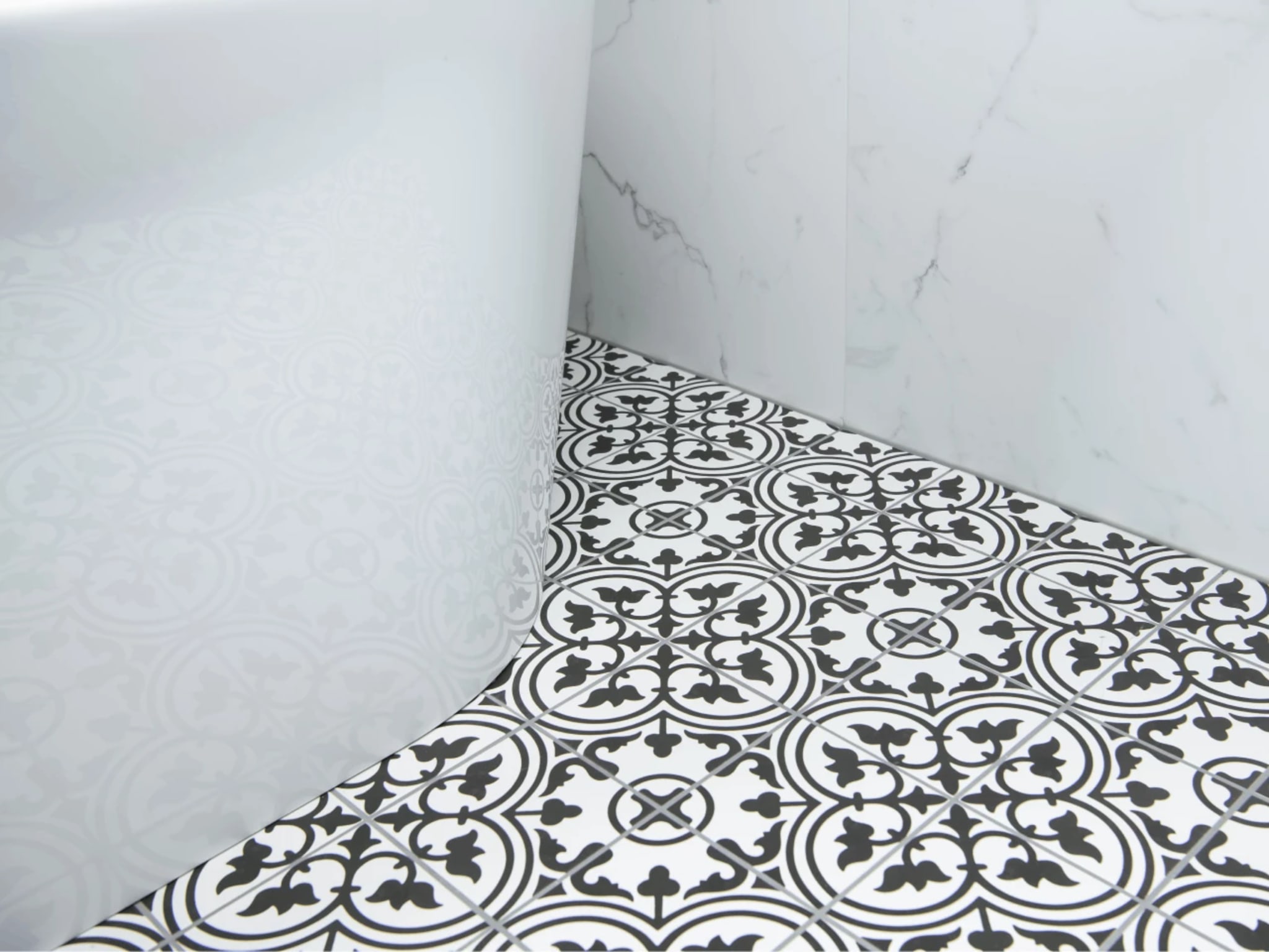 Zwart-witte decortegels met uniek patroon naast het witte ligbad en marmerlook wandtegels
