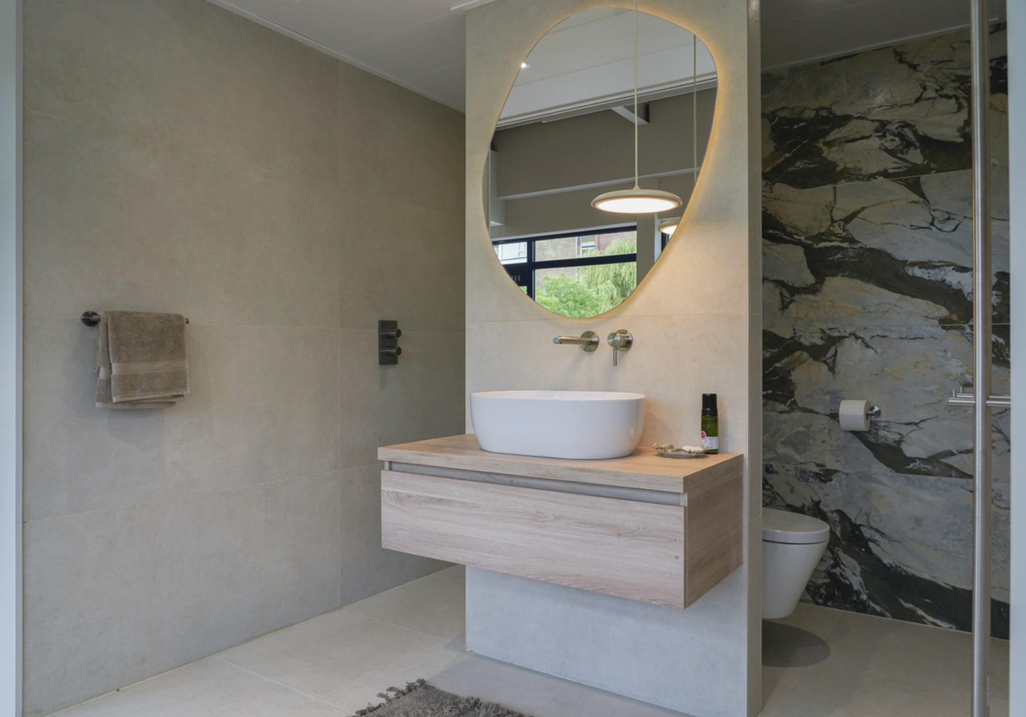 Het licht eiken badmeubel van de Mineral Sage met ovale opzetwastafel, met het hangtoilet en de inloopdouche ernaast