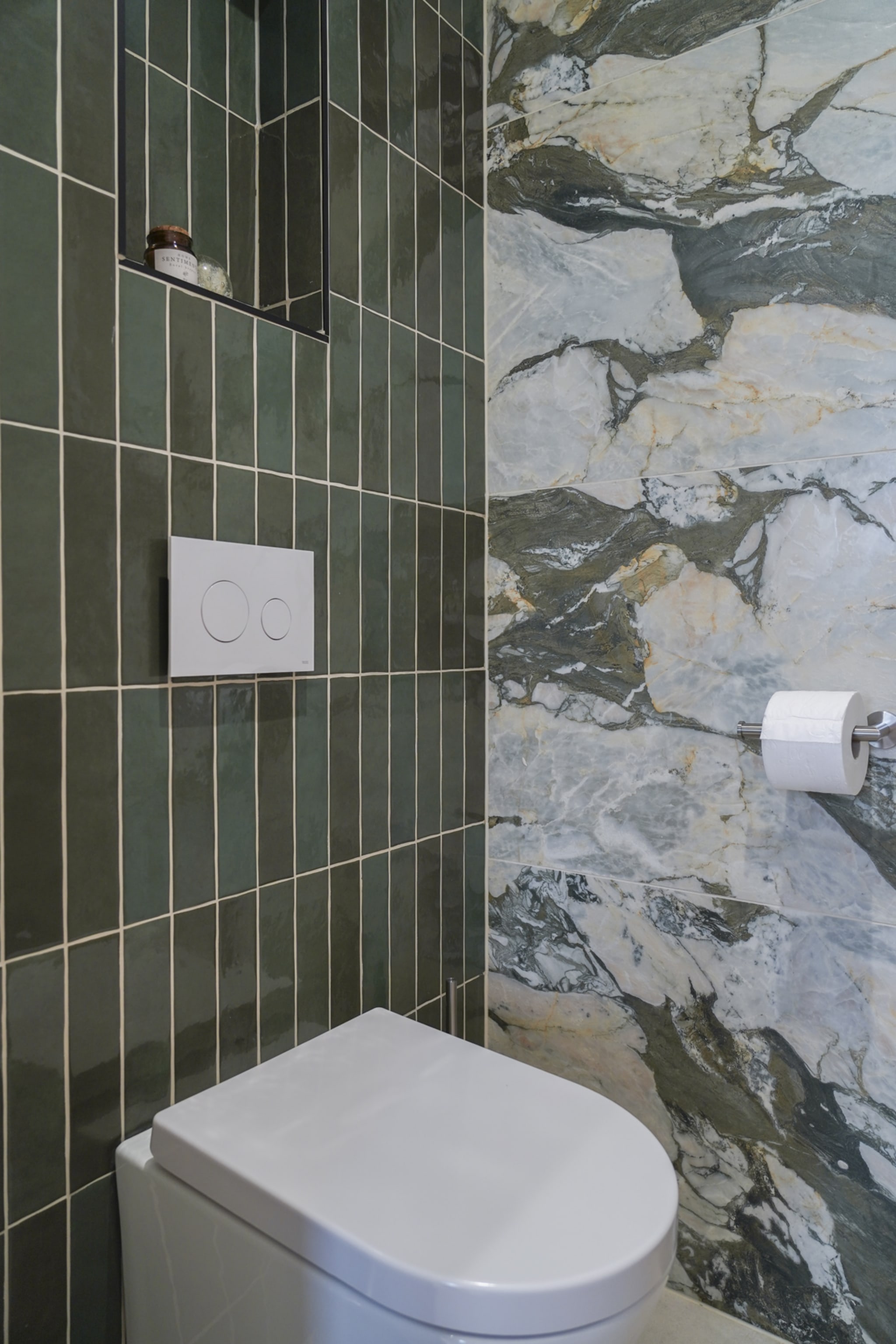 Het hangtoilet van de Mineral Sage tegen diepgroene verticale tegels, naast de marmeren accentwand