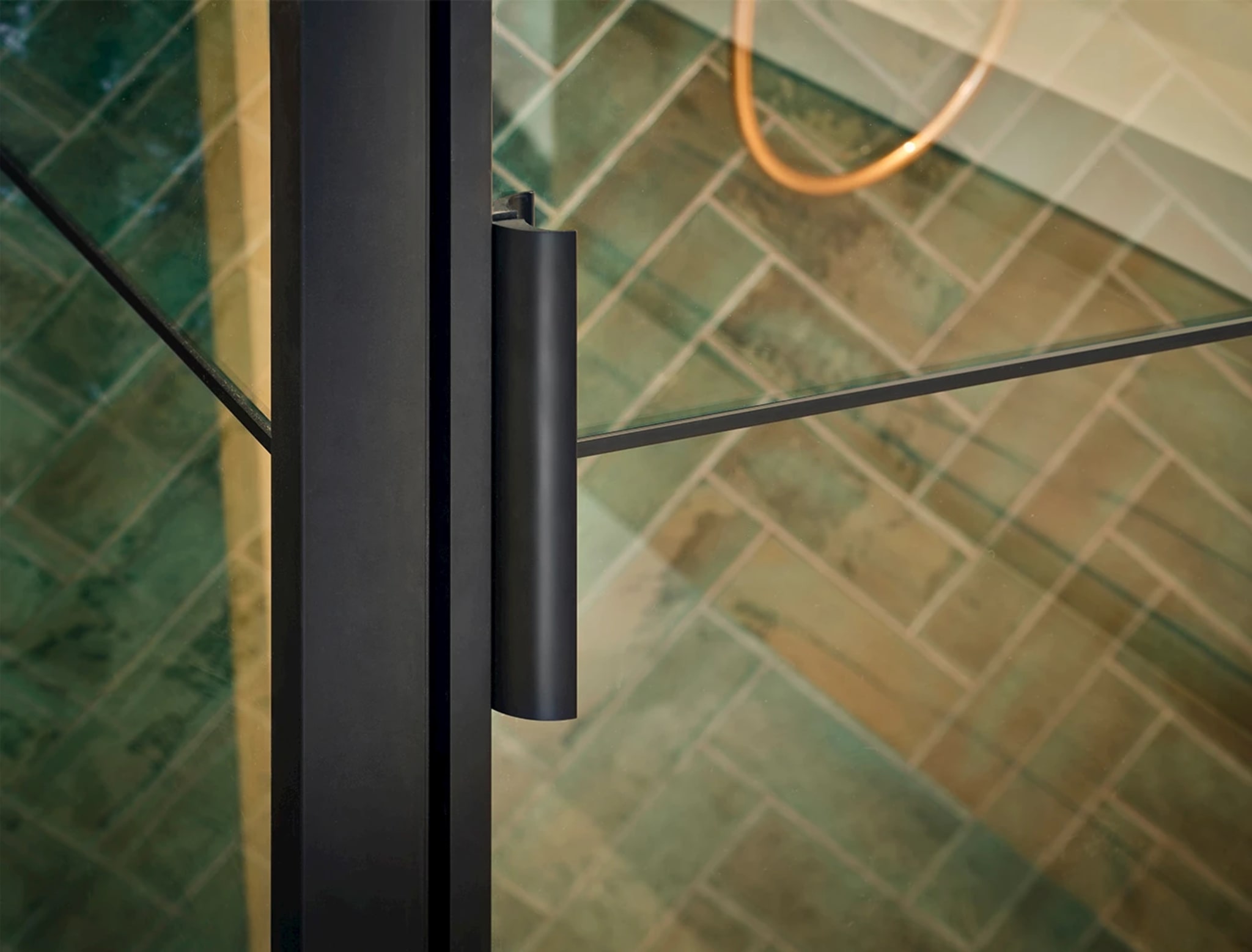 Detail van de mat zwarte greep en het zwarte frame van de glazen douchedeur