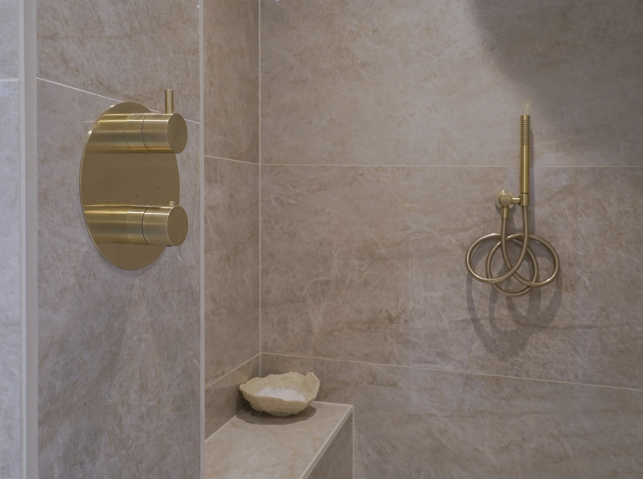 Gouden inbouw thermostaatkraan en handdouche in de inloopdouche van de Taj Mahal, met een tegelbank
