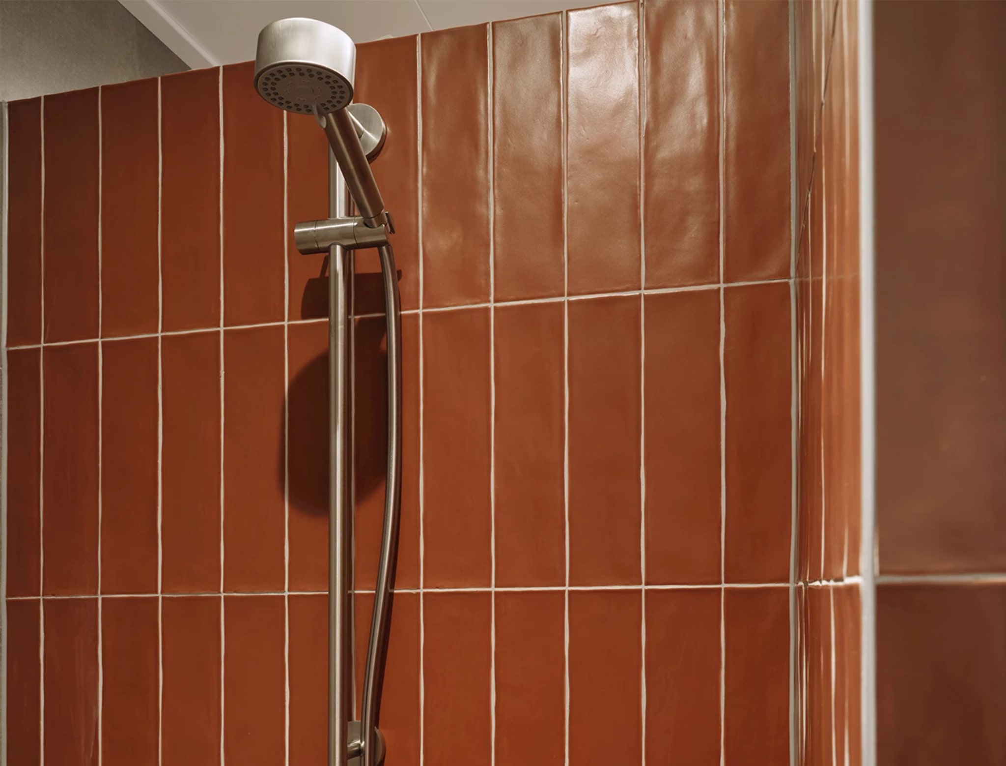 Handdouche in rvs op een glijstang tegen de terracotta tegels van de doucheruimte