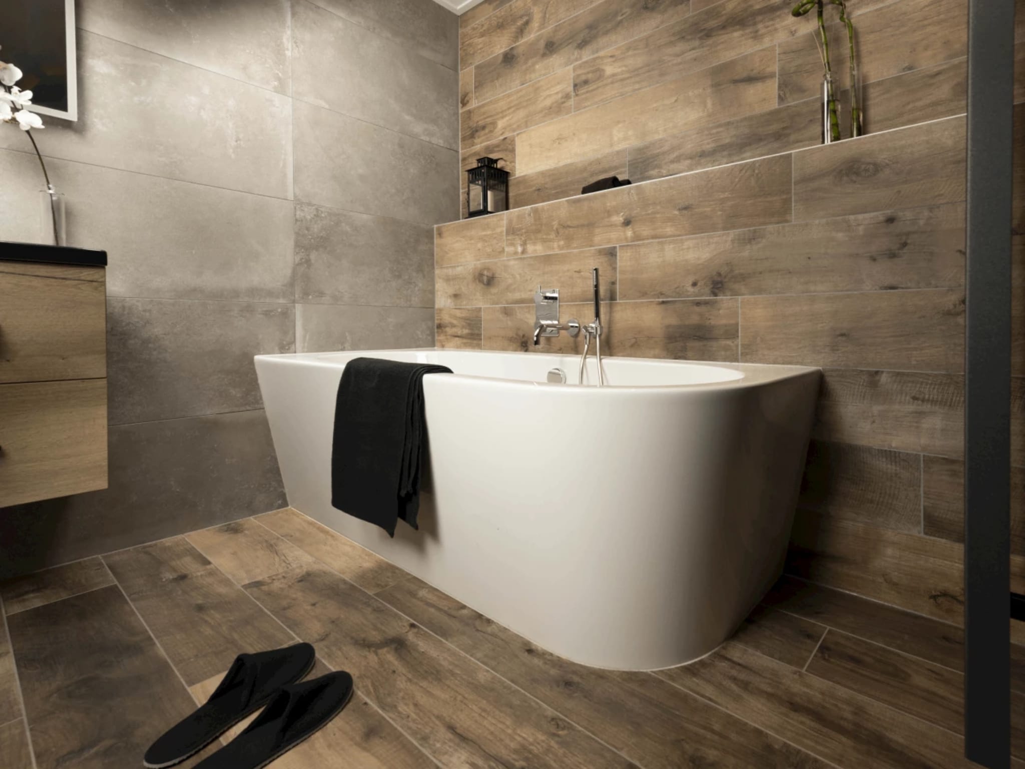 Half vrijstaand wit ligbad met chromen inbouw badkraan tegen houtlook wandtegels