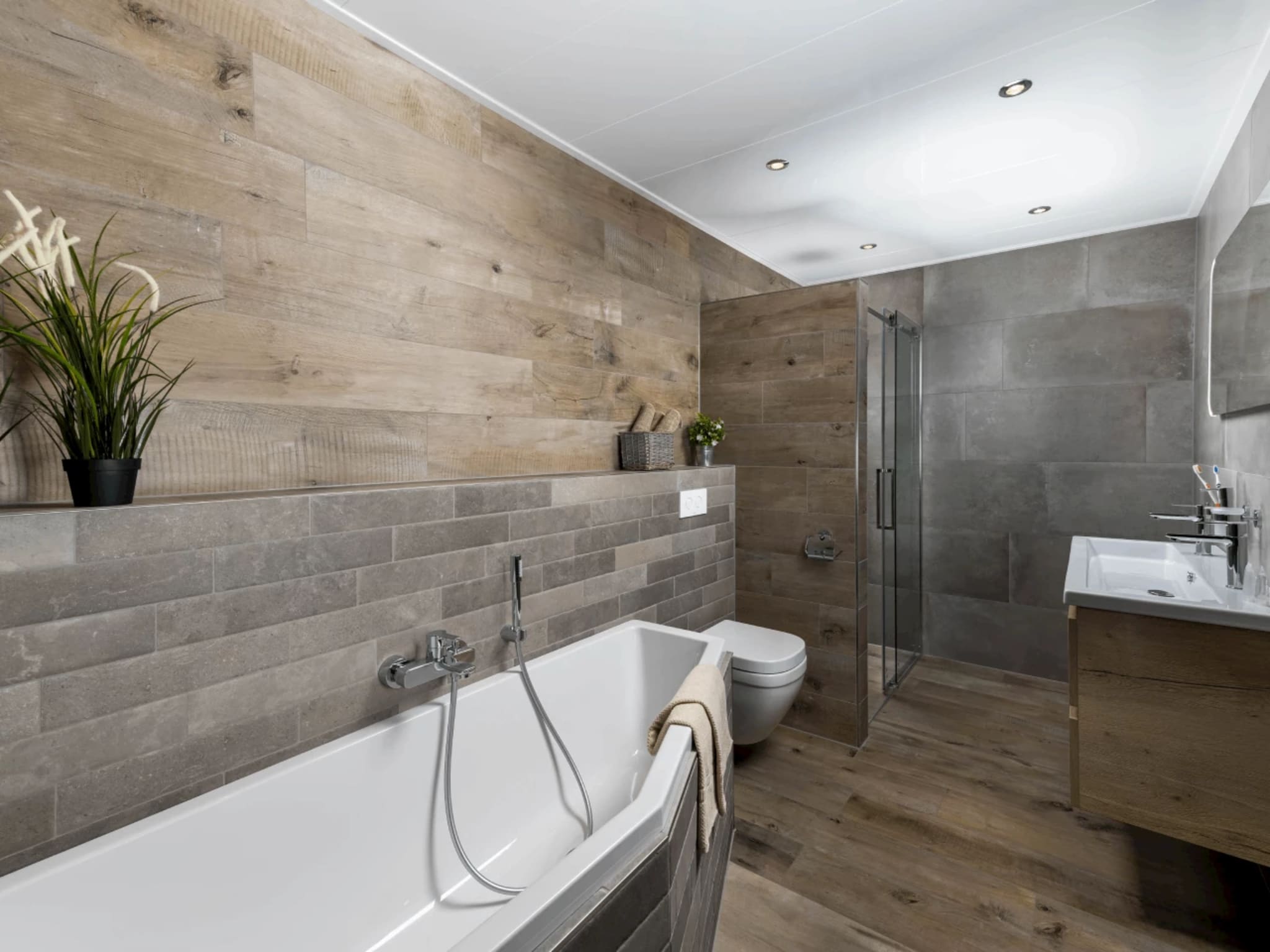 Badkamer met ligbad, douche met deur en houtlook tegels gecombineerd met betonlook