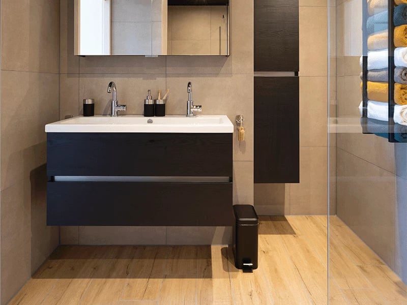 Moderne badkamer met houtlook vloertegels, donker badmeubel en een inloopdouche met glazen wand