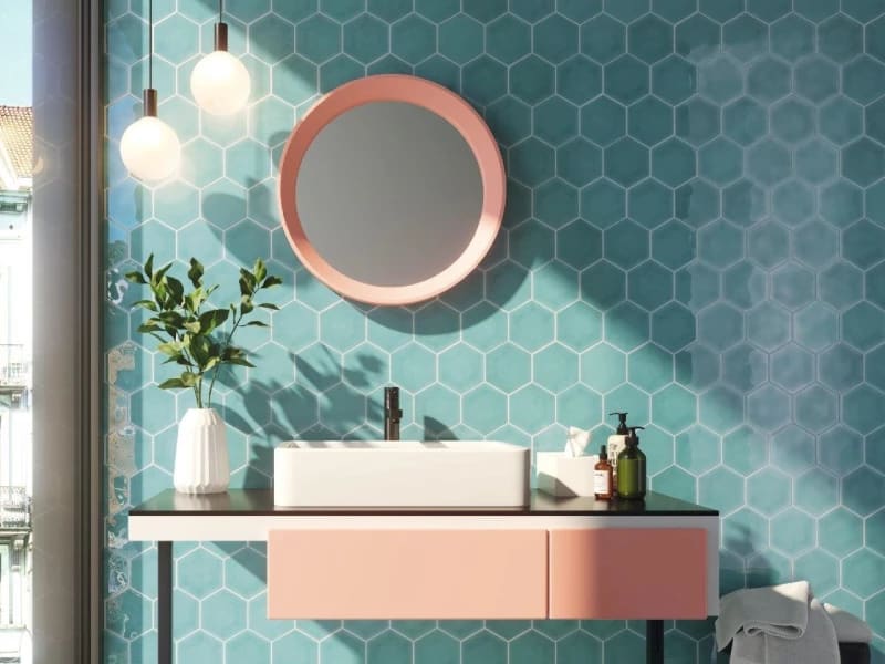 Badkamer met turquoise hexagon wandtegels, een zalmroze badmeubel en een spiegel met roze lijst