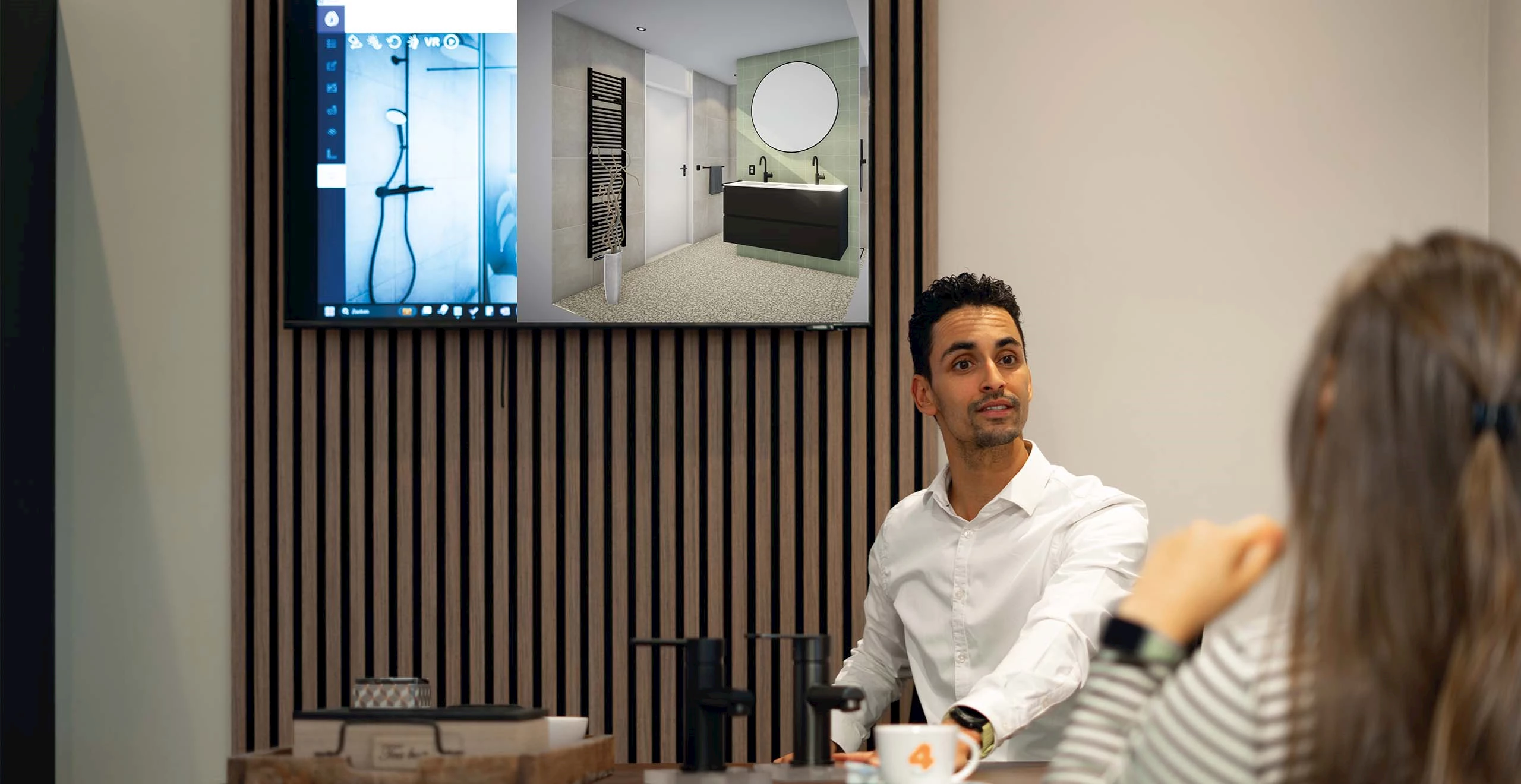 Badkameradviseur in gesprek met een klant, met het 3D-ontwerpprogramma op het scherm achter hem